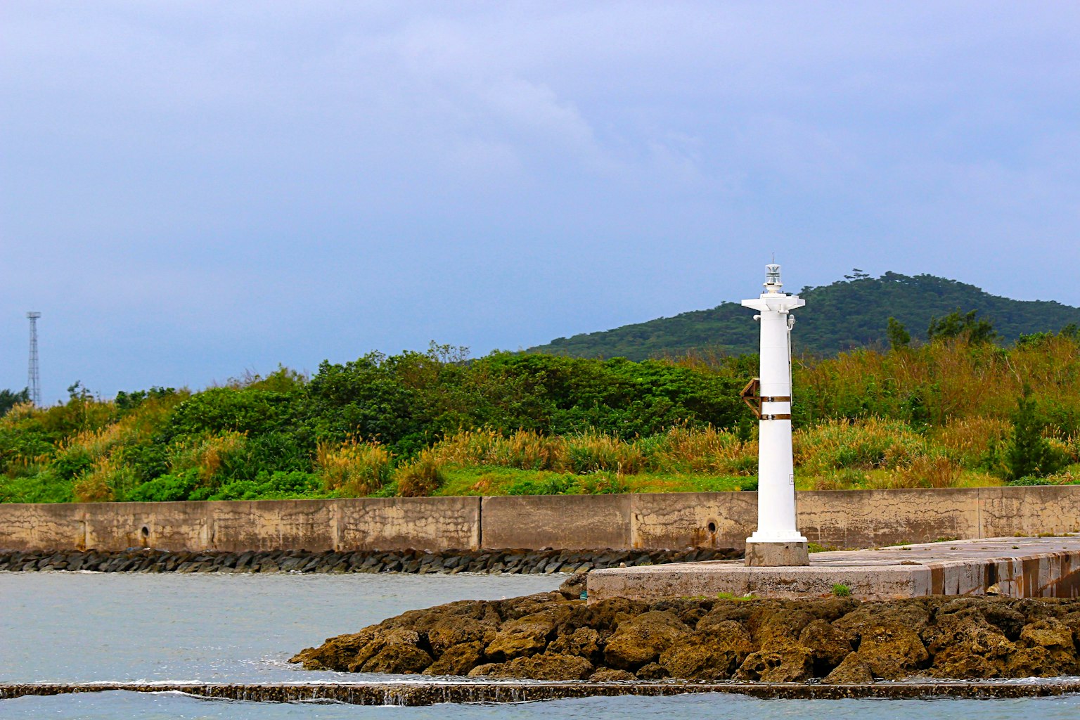 Faro bianco sulla costa con colline verdi sullo sfondo