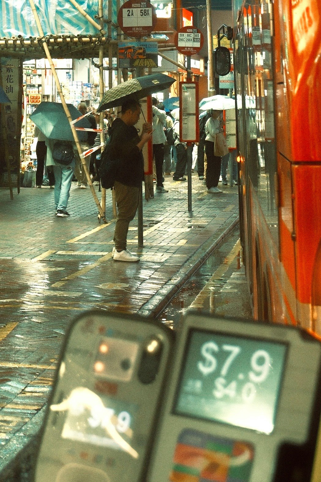 Menschen mit Regenschirmen in einer regen­nassen Einkaufs­gasse mit Ladenschildern