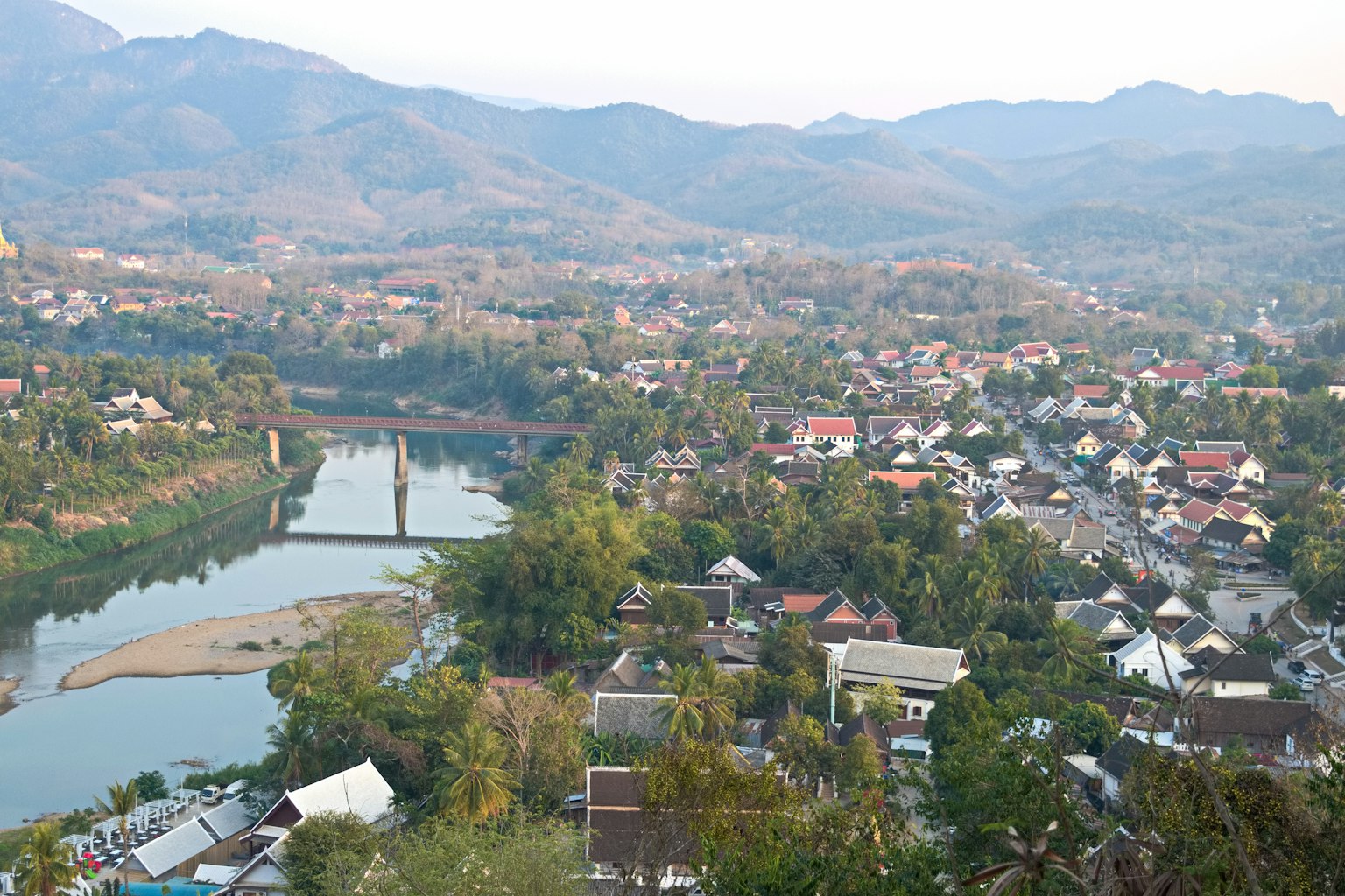 Vista escénica de un pueblo rodeado de montañas con un río y un puente