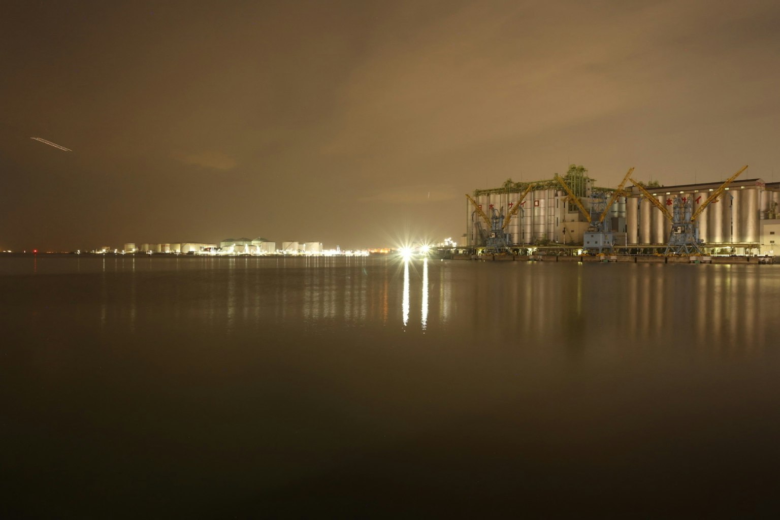 Silhouette di un impianto industriale riflessa sull'acqua calma di notte