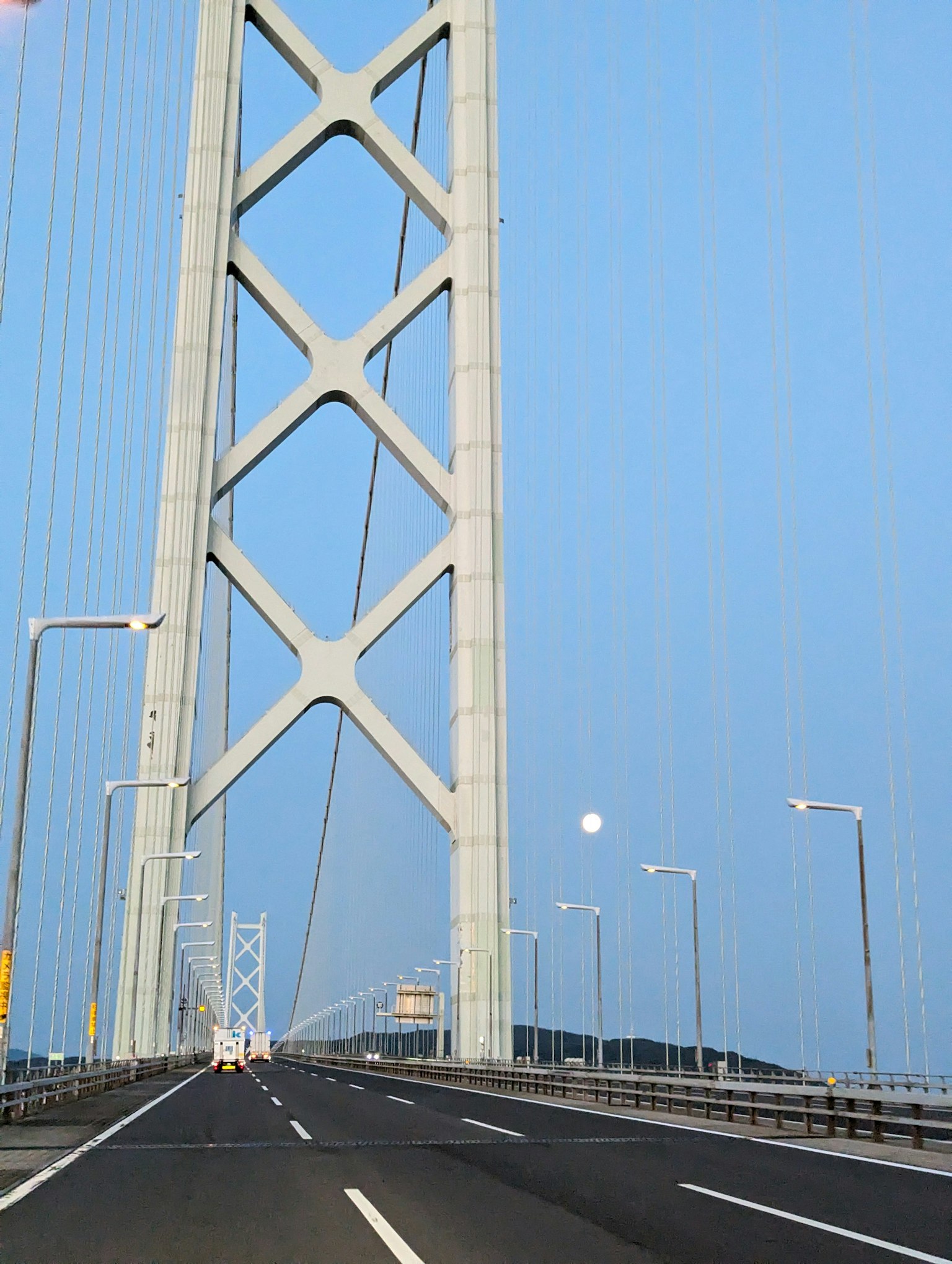 Struktur penyangga jembatan di bawah langit biru dengan bulan terlihat