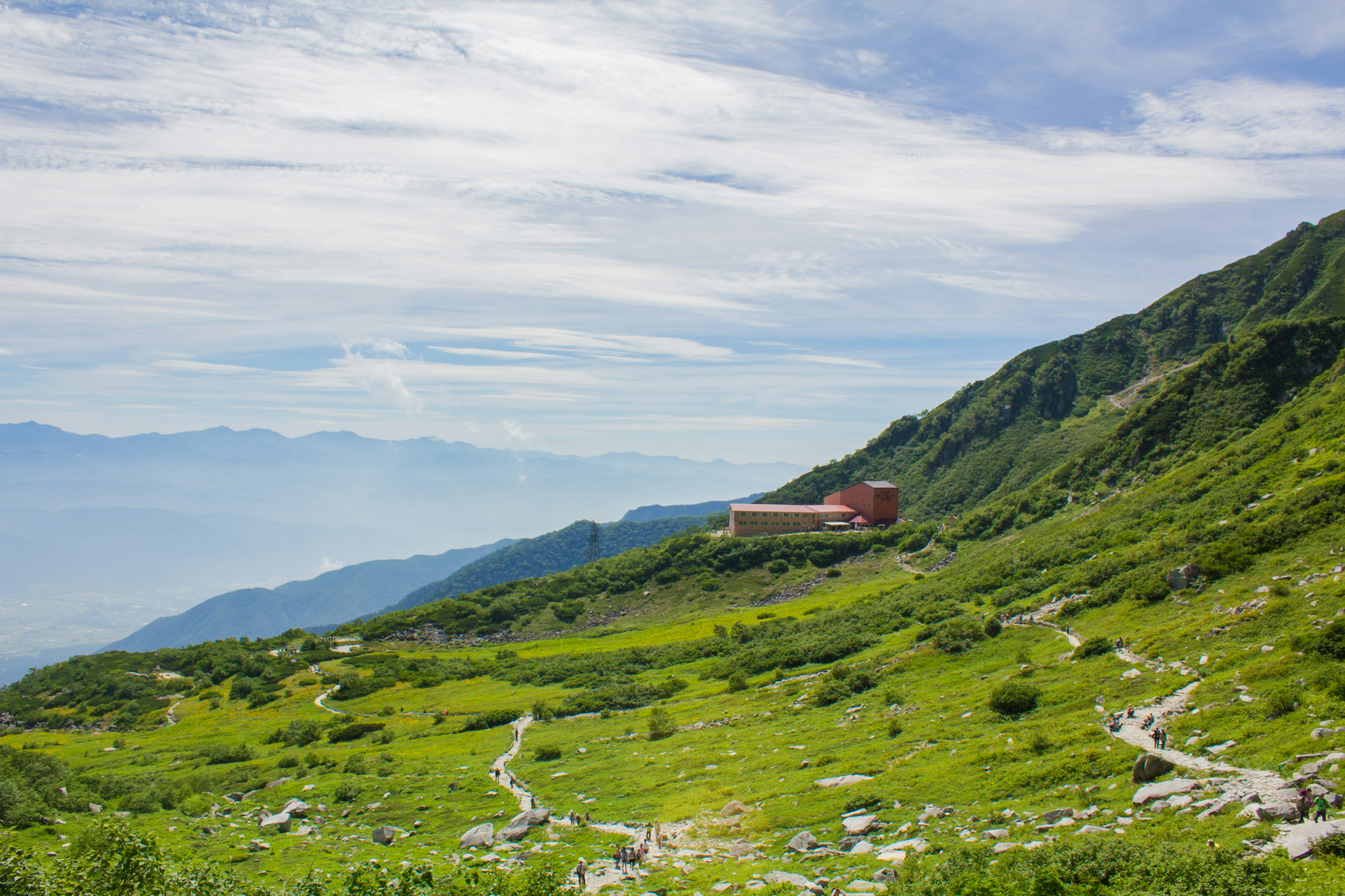緑の山腹に続く小道と小屋のある風景
