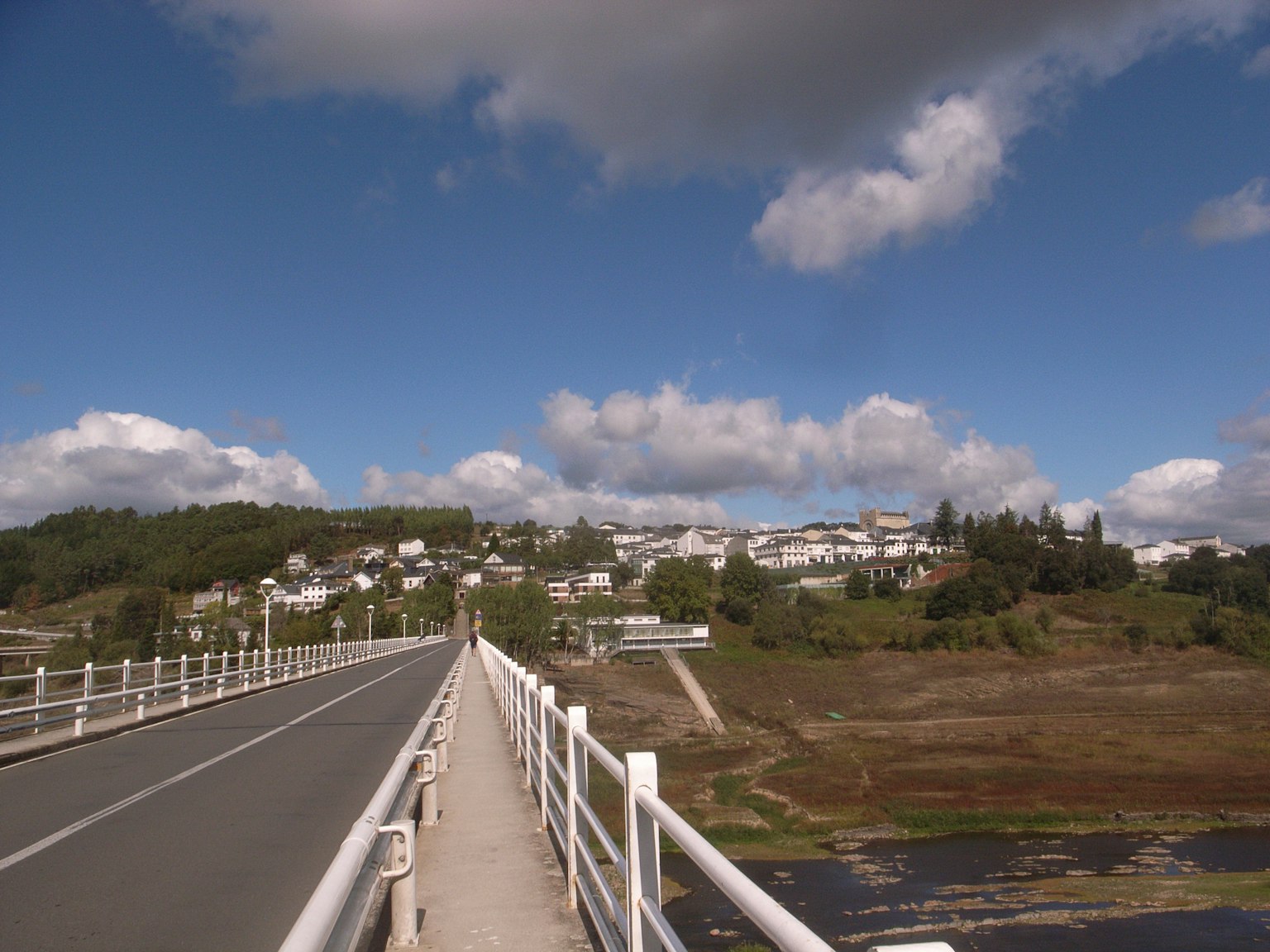 Malersiche Ansicht einer Brücke mit weißen Geländern unter einem blauen Himmel und flauschigen Wolken