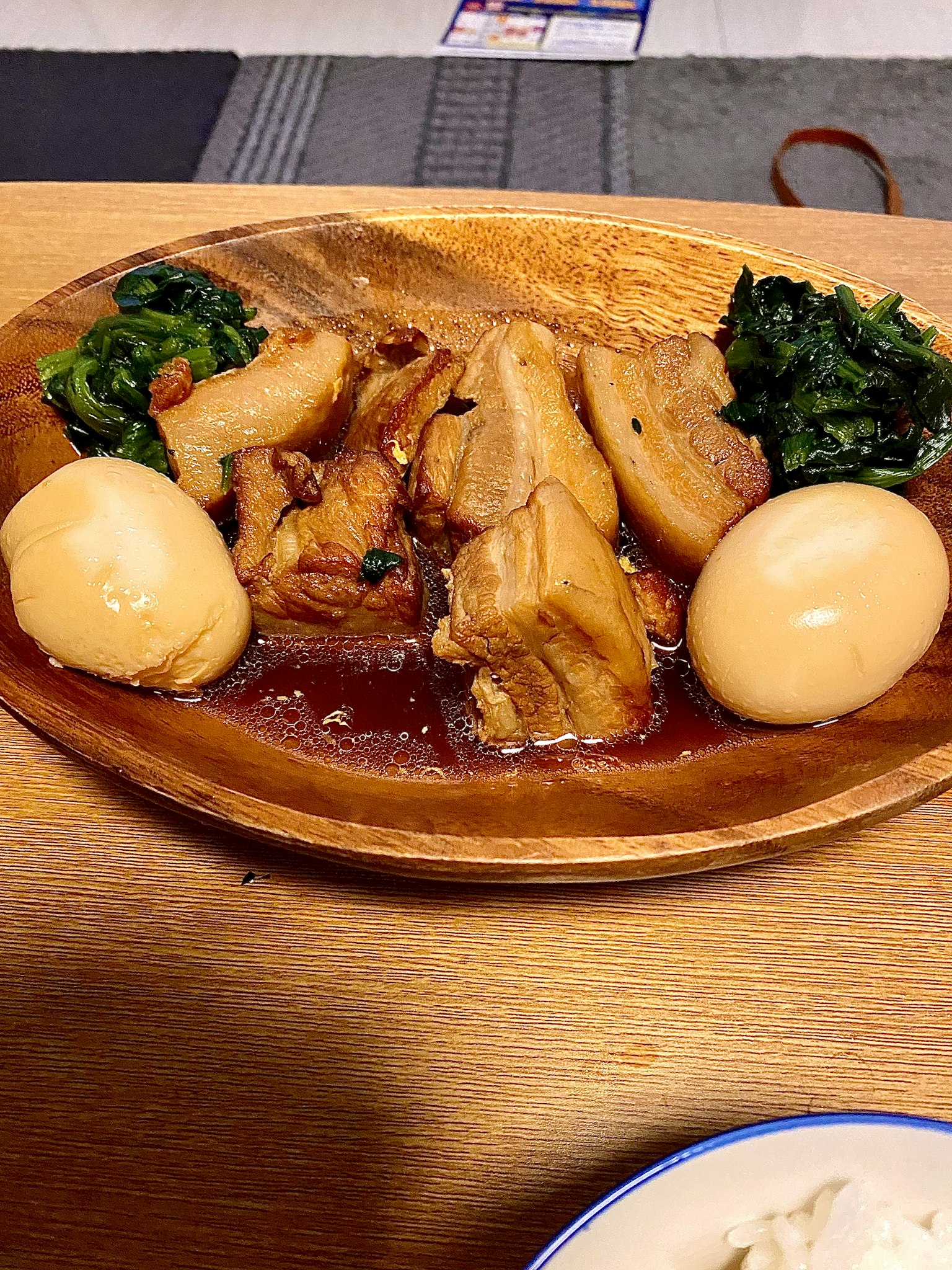 Gericht auf einem Holztablett mit Fleisch und Eiern, begleitet von grünen Gemüse und einer reichhaltigen Sauce