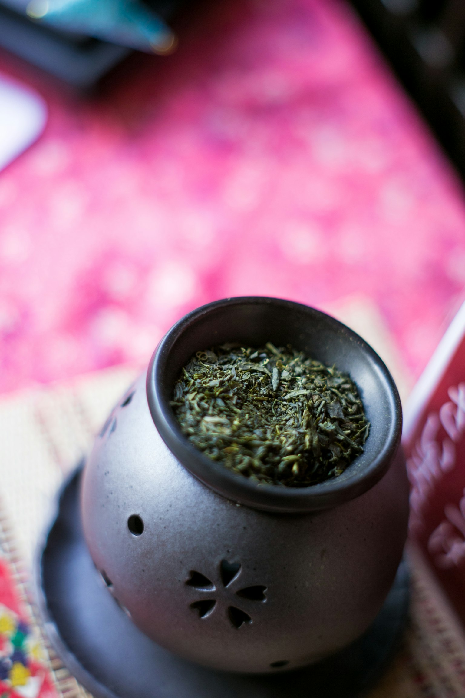 一个装满绿茶叶的茶壶，背景是粉色布料