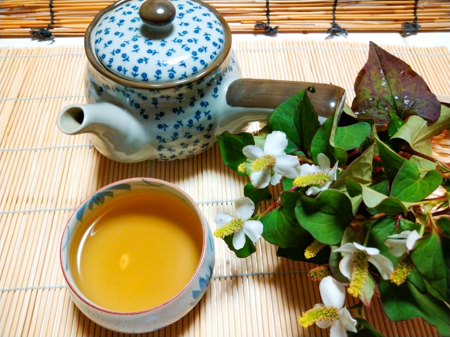 蓝色图案茶壶与茶和花放在竹席上