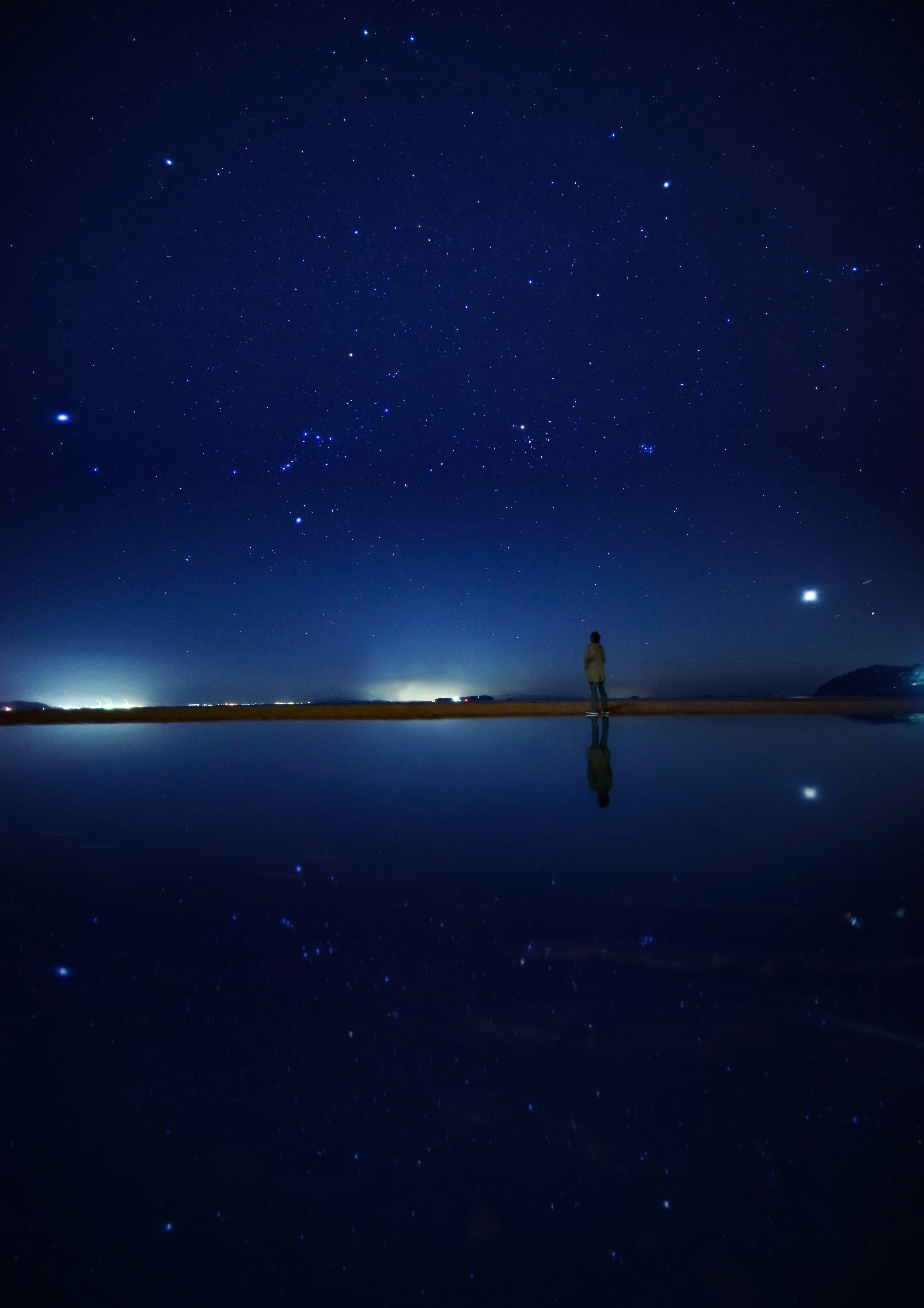 水鏡に映る星空と静かな海辺の夜景