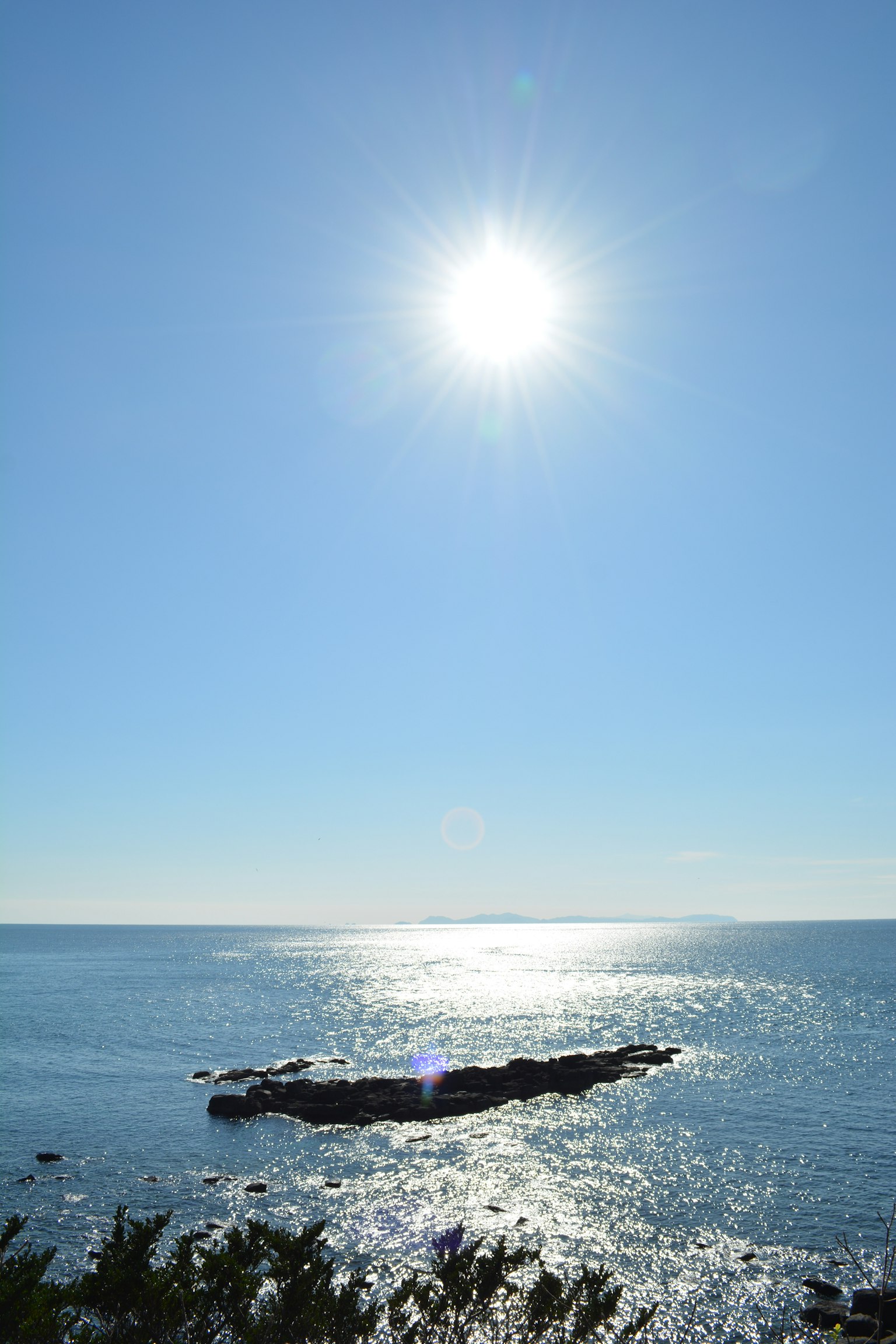 Sole luminoso su un oceano blu sereno con una costa rocciosa