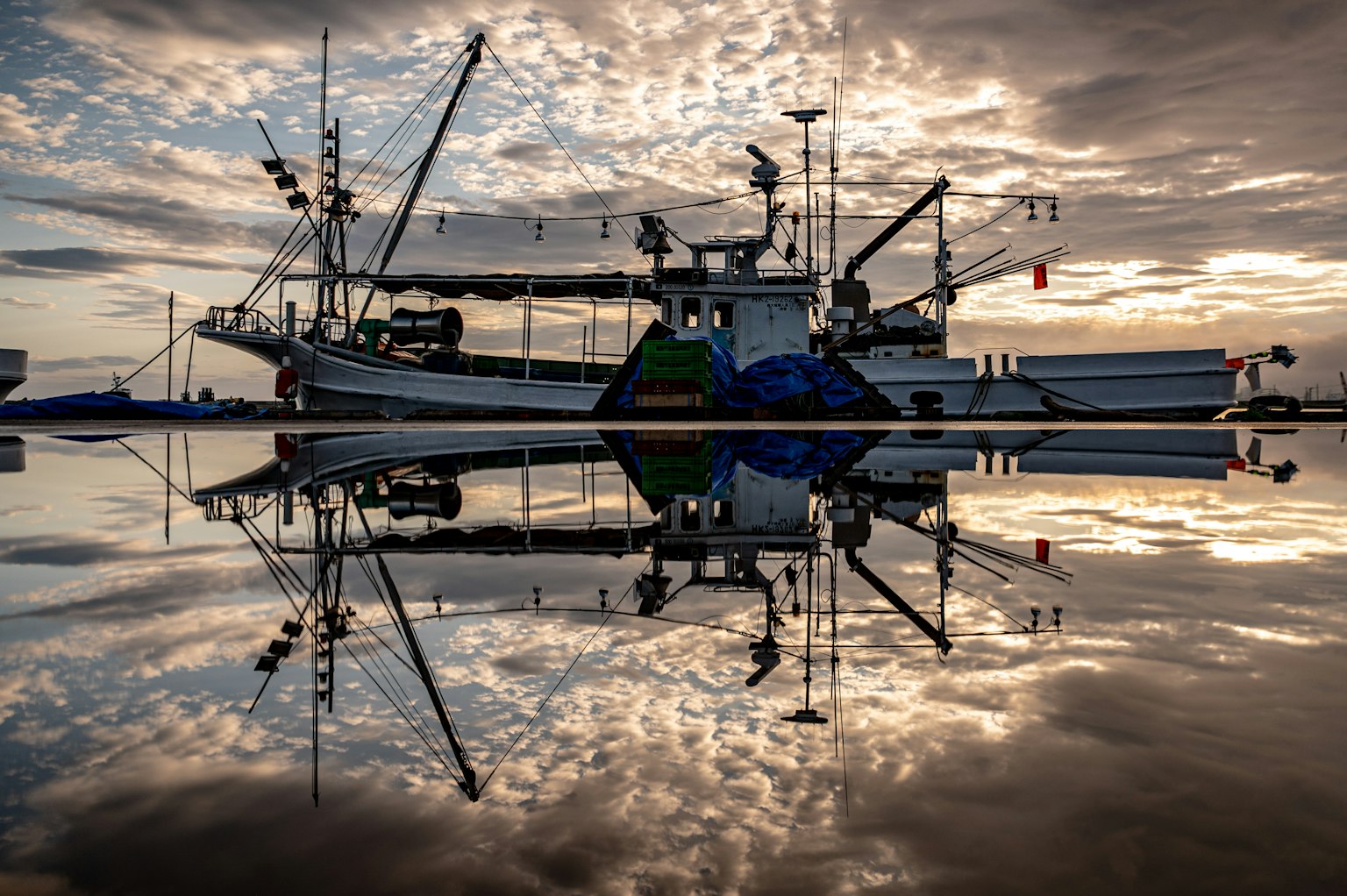 Silhouette di un peschereccio riflesso sull'acqua con nuvole drammatiche al tramonto