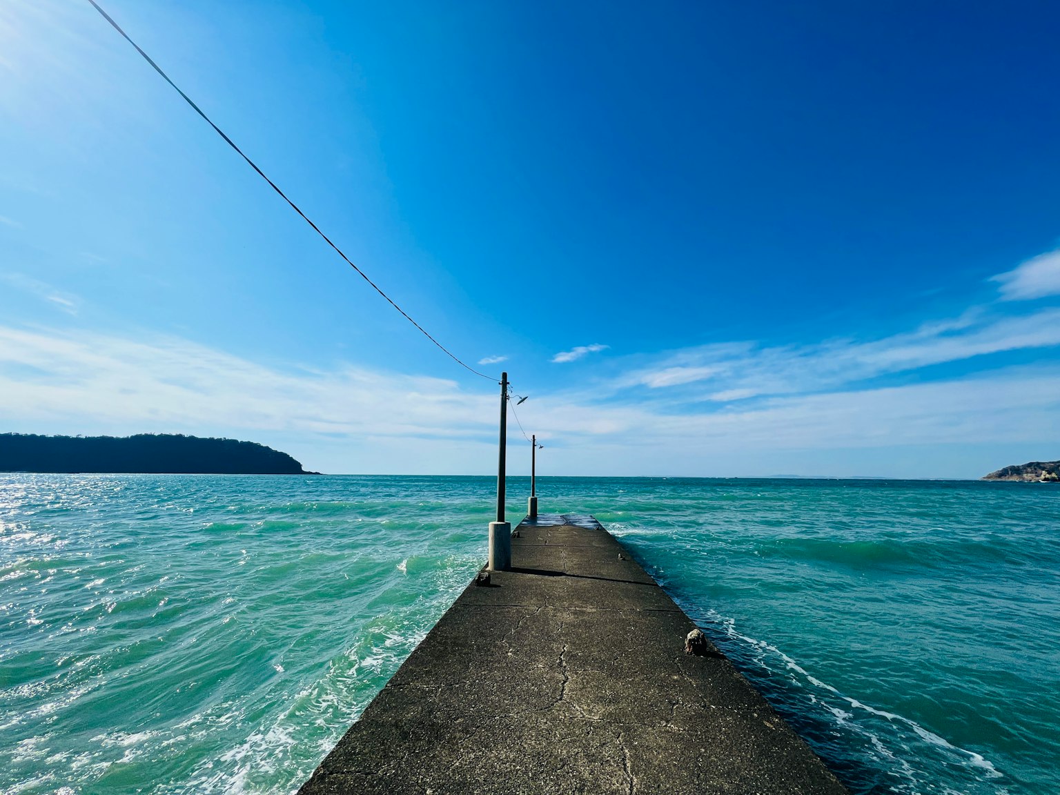 Molo in cemento che si estende nell'acqua turchese sotto un cielo blu chiaro
