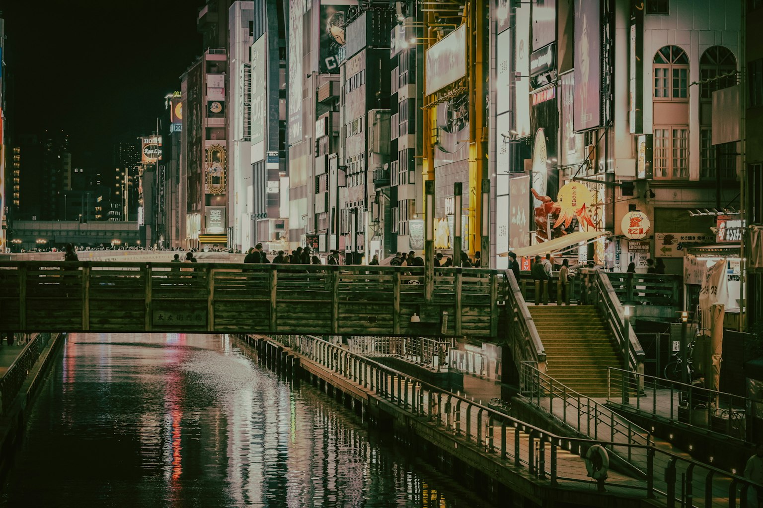 Lebendige Stadtlandschaft bei Nacht mit hellen Gebäuden entlang des Flusses und einer Brücke
