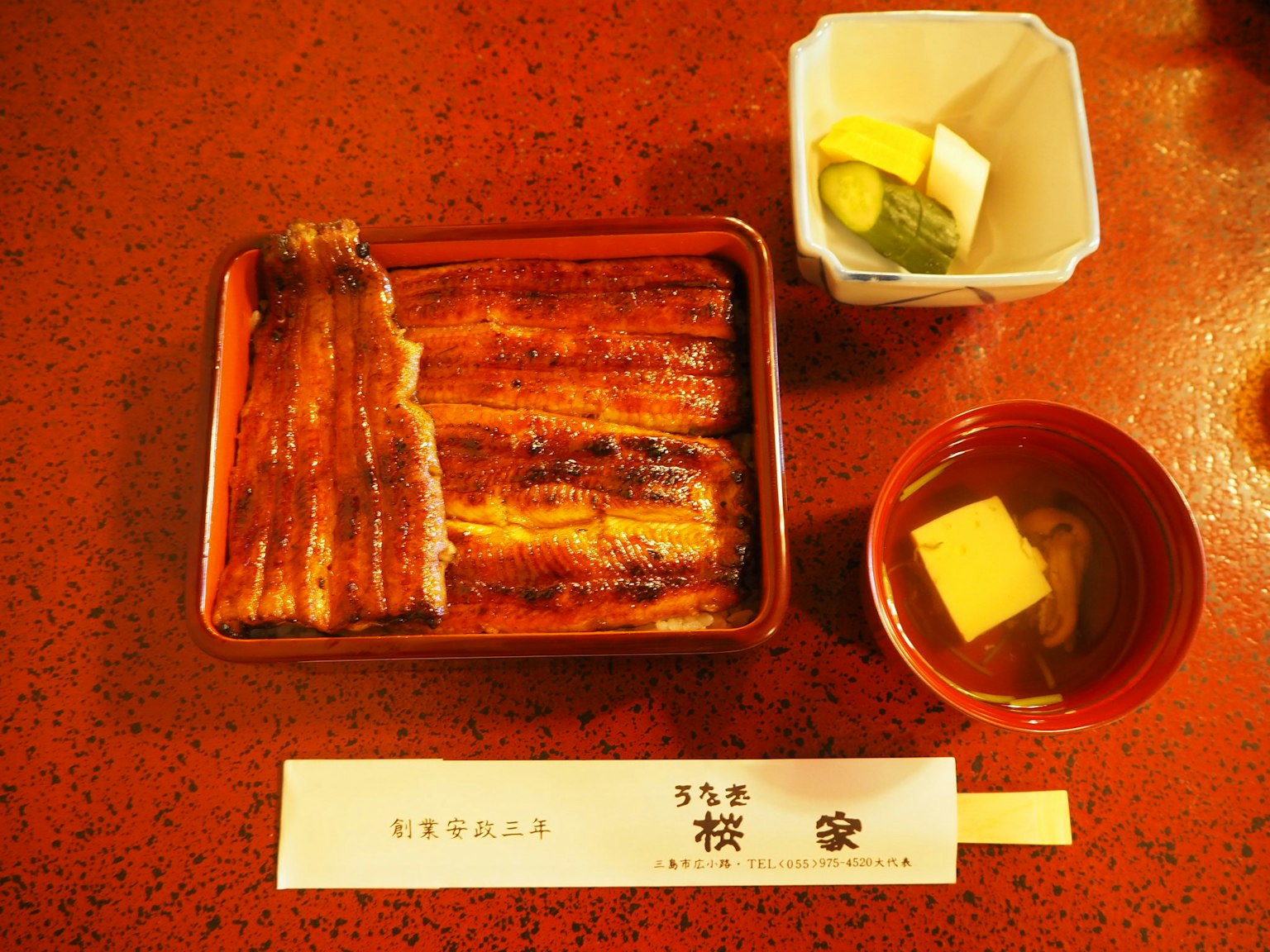 Anguila a la parrilla en un plato rojo con sopa de miso y encurtidos