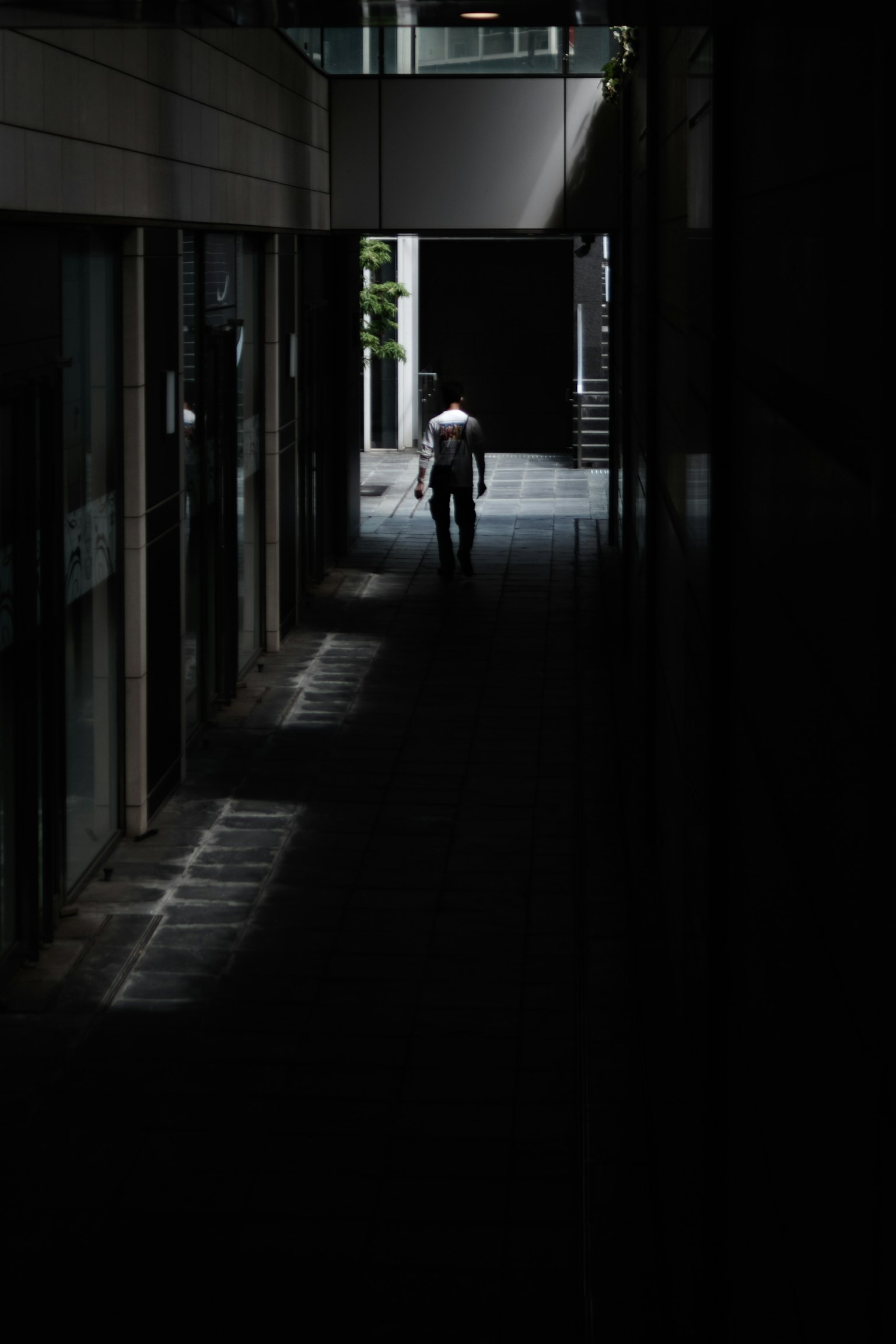Une silhouette marchant dans un couloir faiblement éclairé avec des contrastes de lumière et d'ombre
