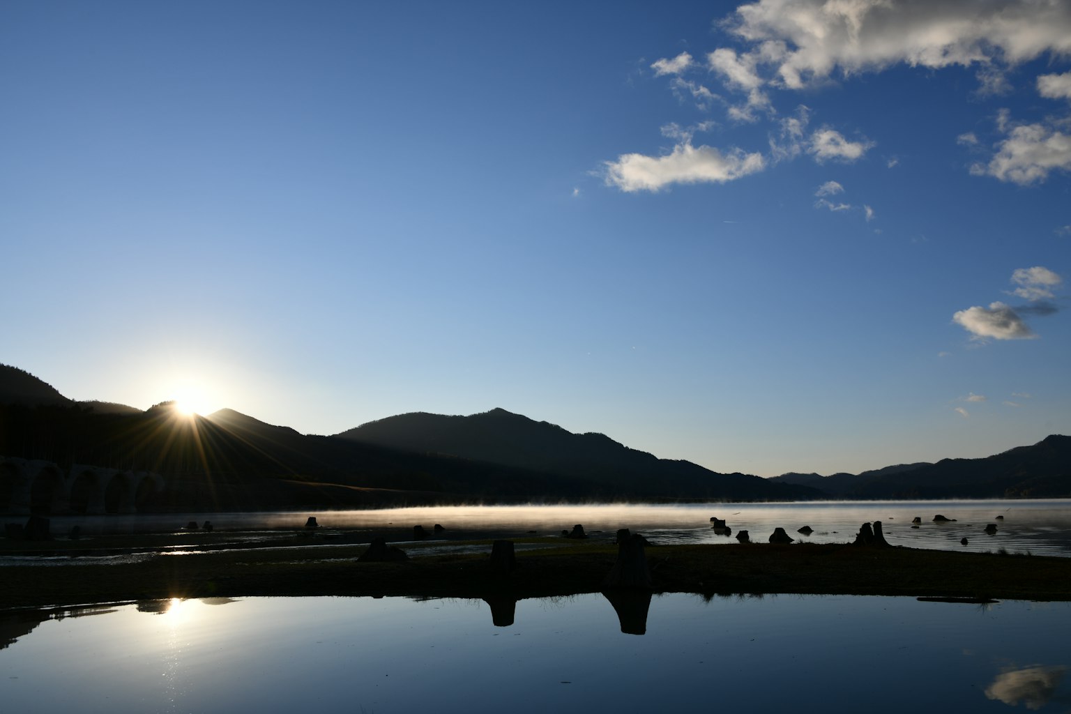 Paisaje sereno de lago con siluetas de montañas al amanecer