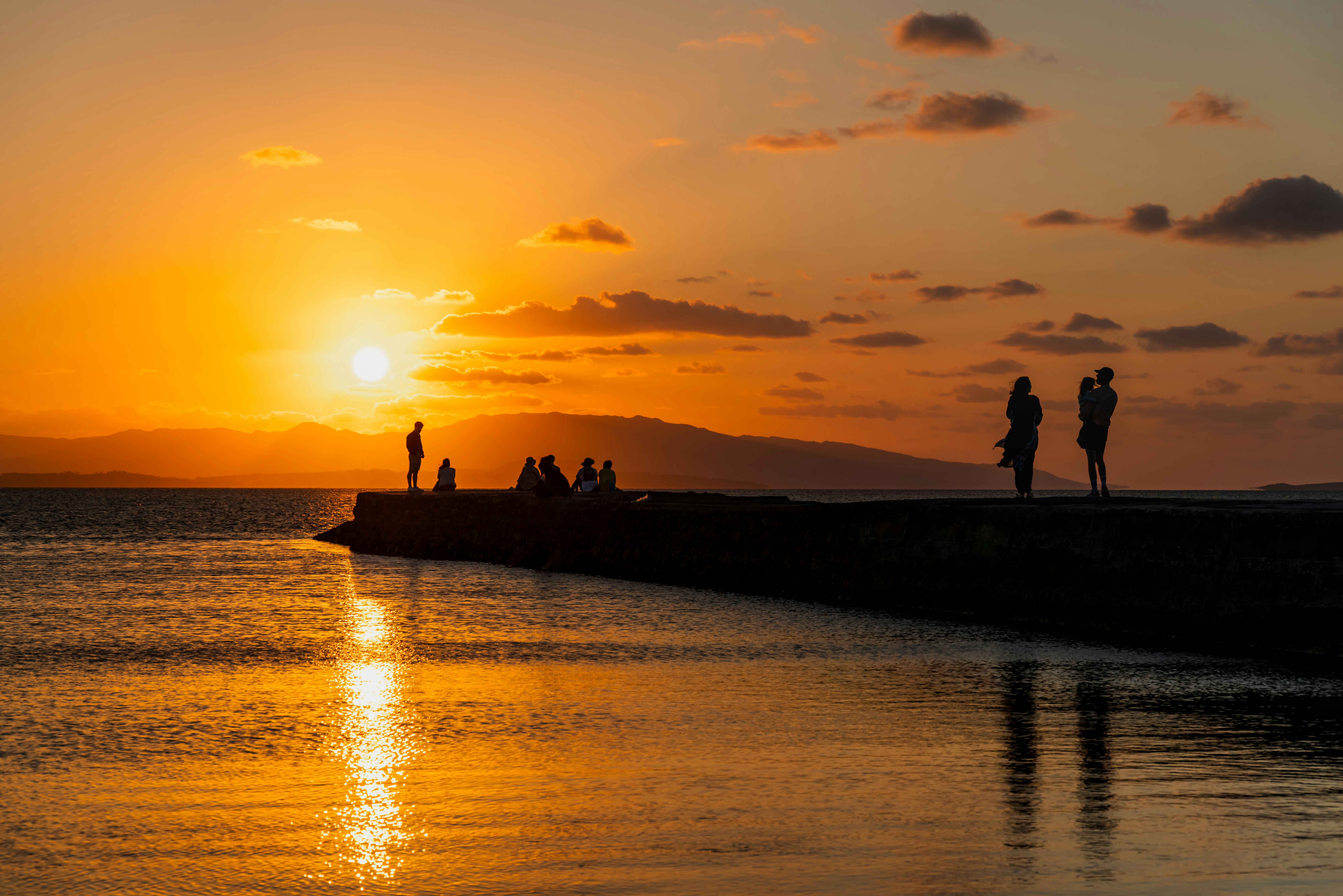 夕日に照らされた海辺の防波堤で人が歩く風景
