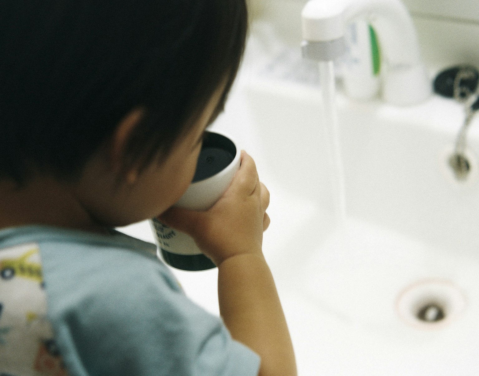 孩子手持杯子在水槽旁喝水