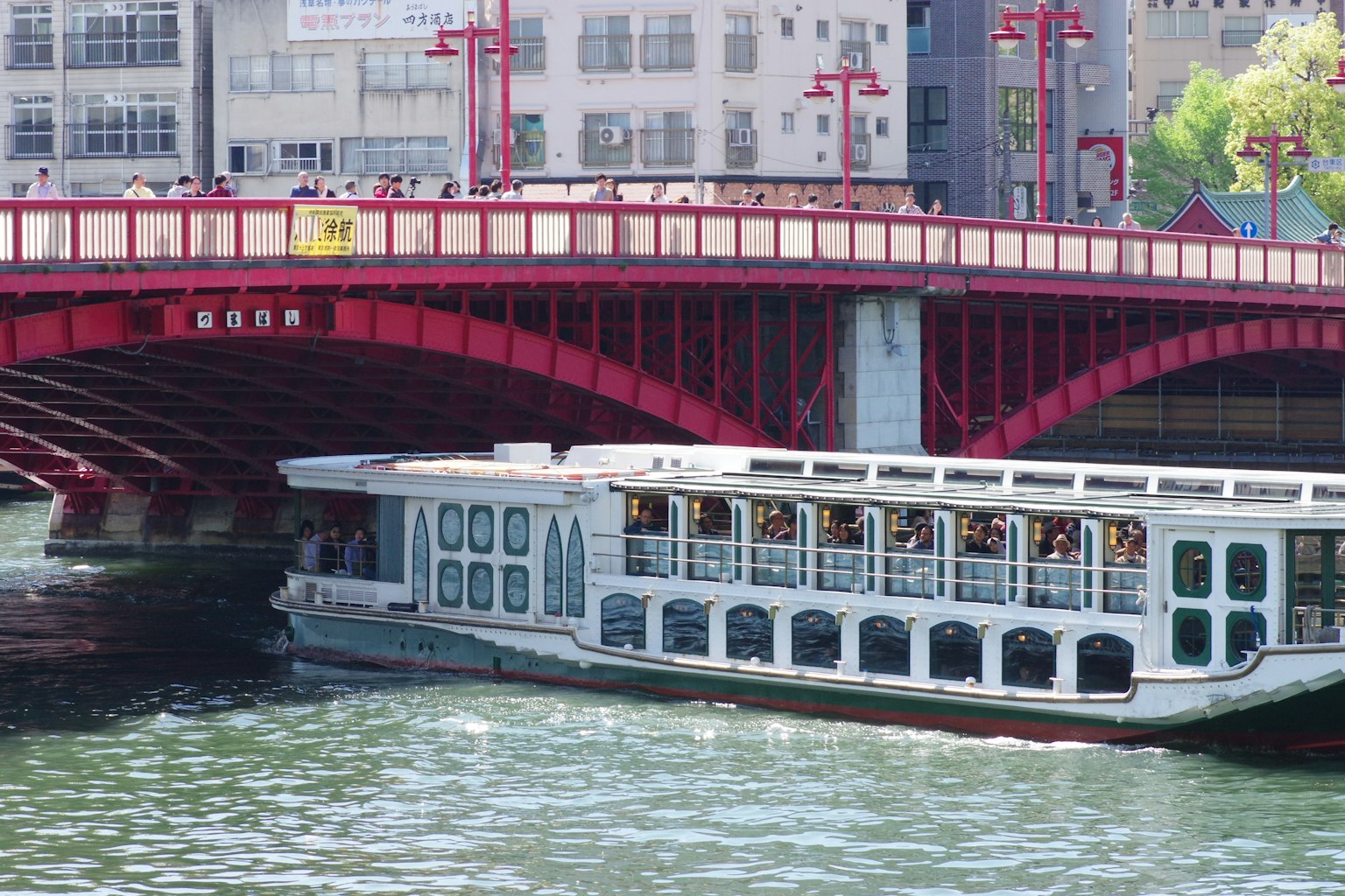 เรือท่องเที่ยวผ่านใต้สะพานสีแดงพร้อมทิวทัศน์แม่น้ำ