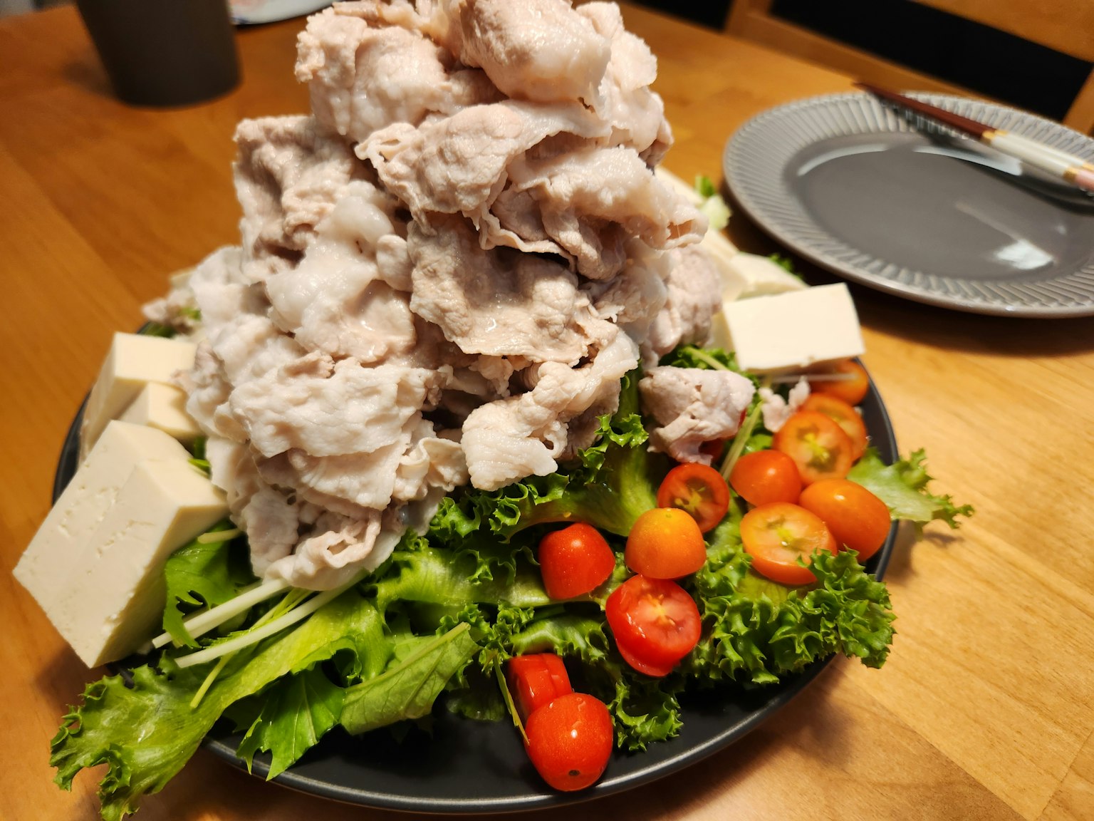 Un plato con una montaña de carne sobre una cama de verduras frescas y tofu