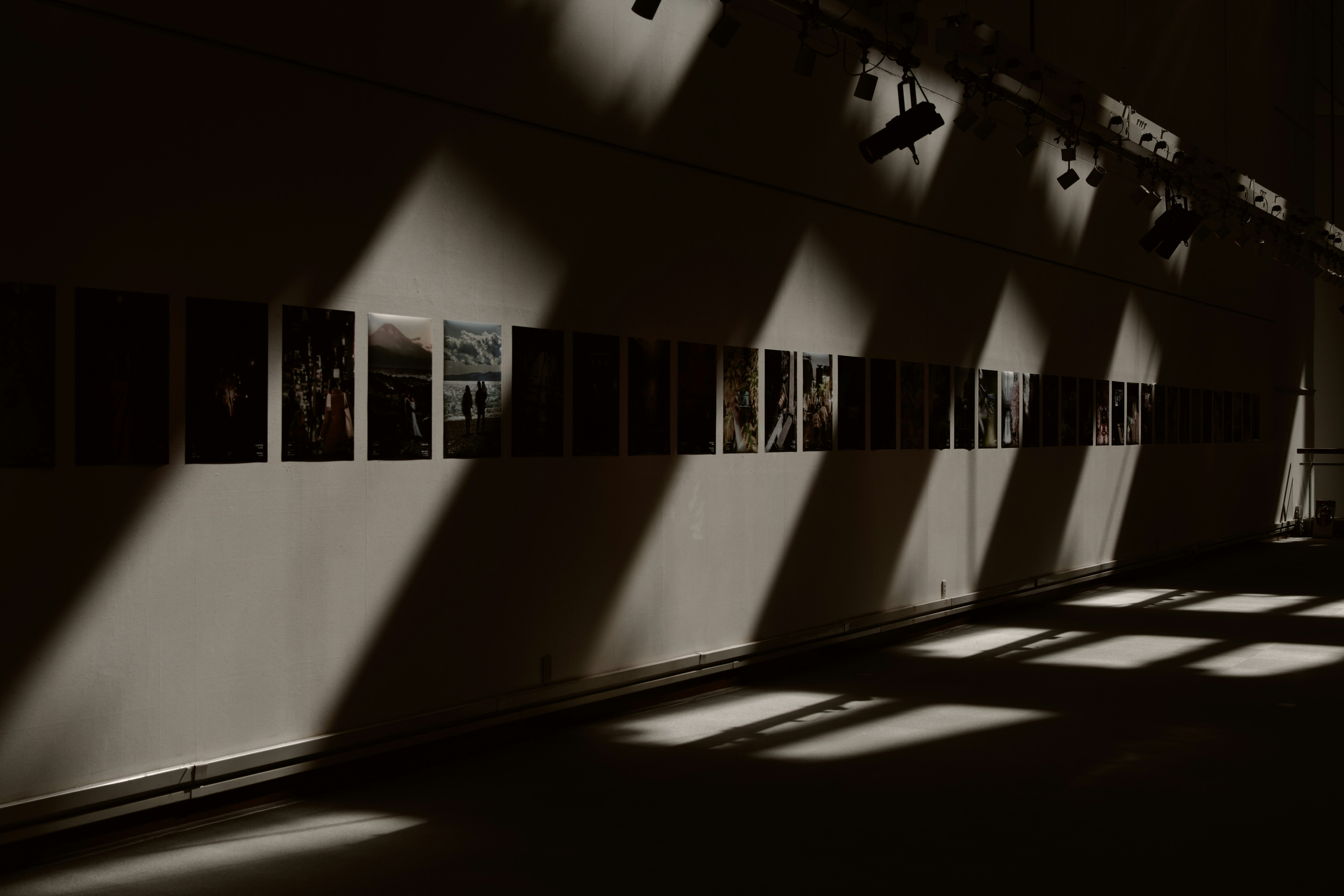天井光の影が落ちる展示会場の壁面と写真パネル