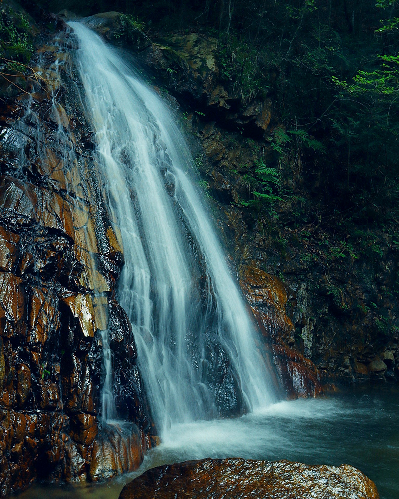 Una bella cascata che scorre giù per scogliere rocciose in un paesaggio verdeggiante