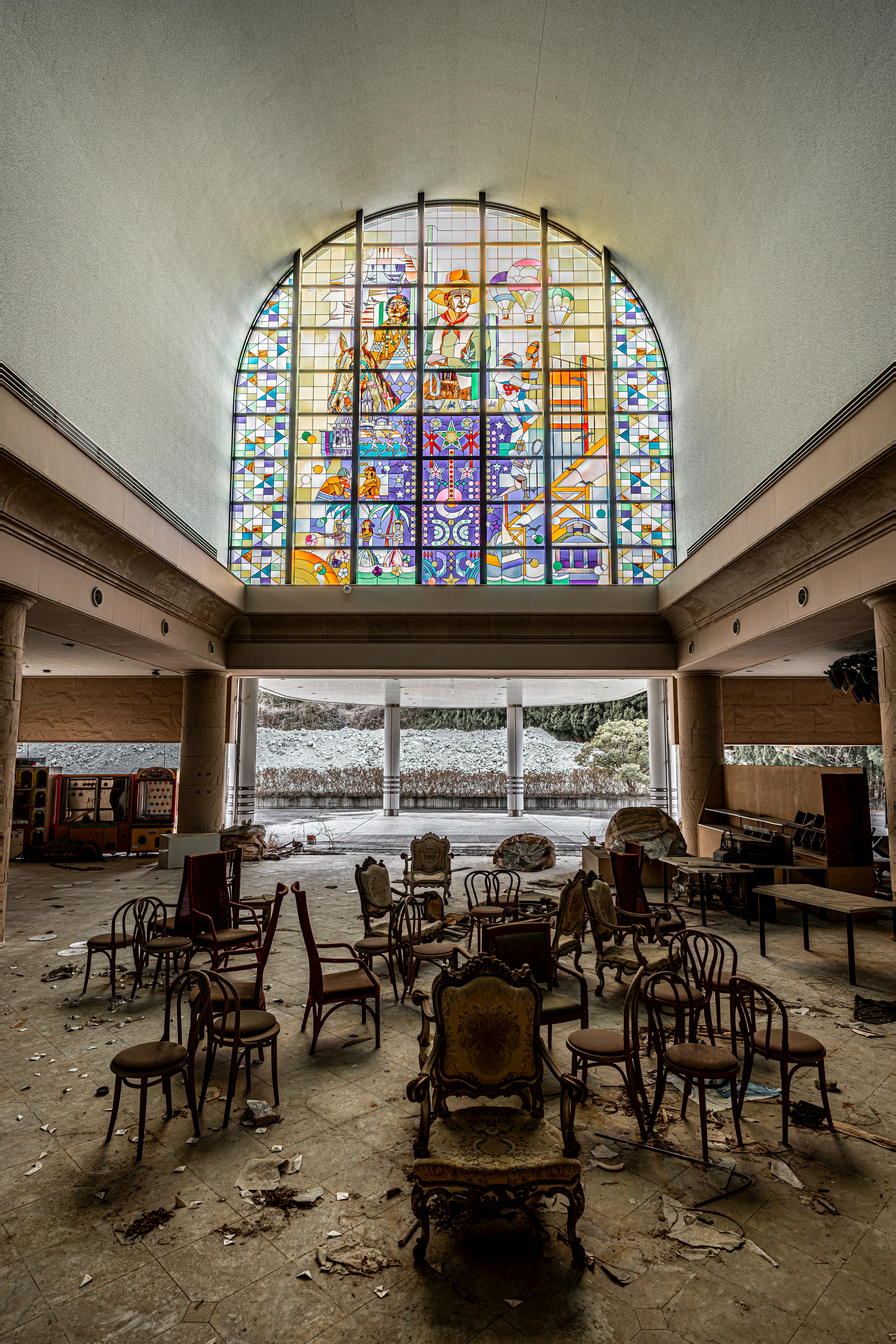 An abandoned-looking interior with rows of chairs and a stained-glass window