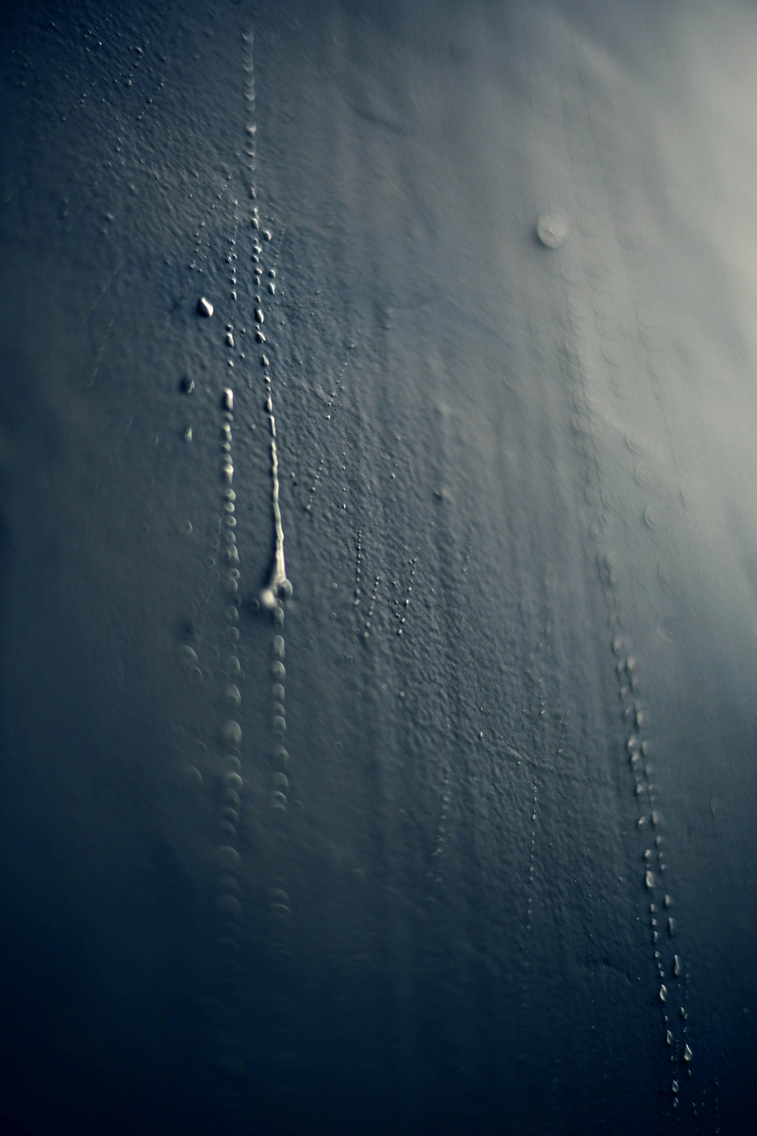 Close-up of a wall with water droplets running down in a dark background