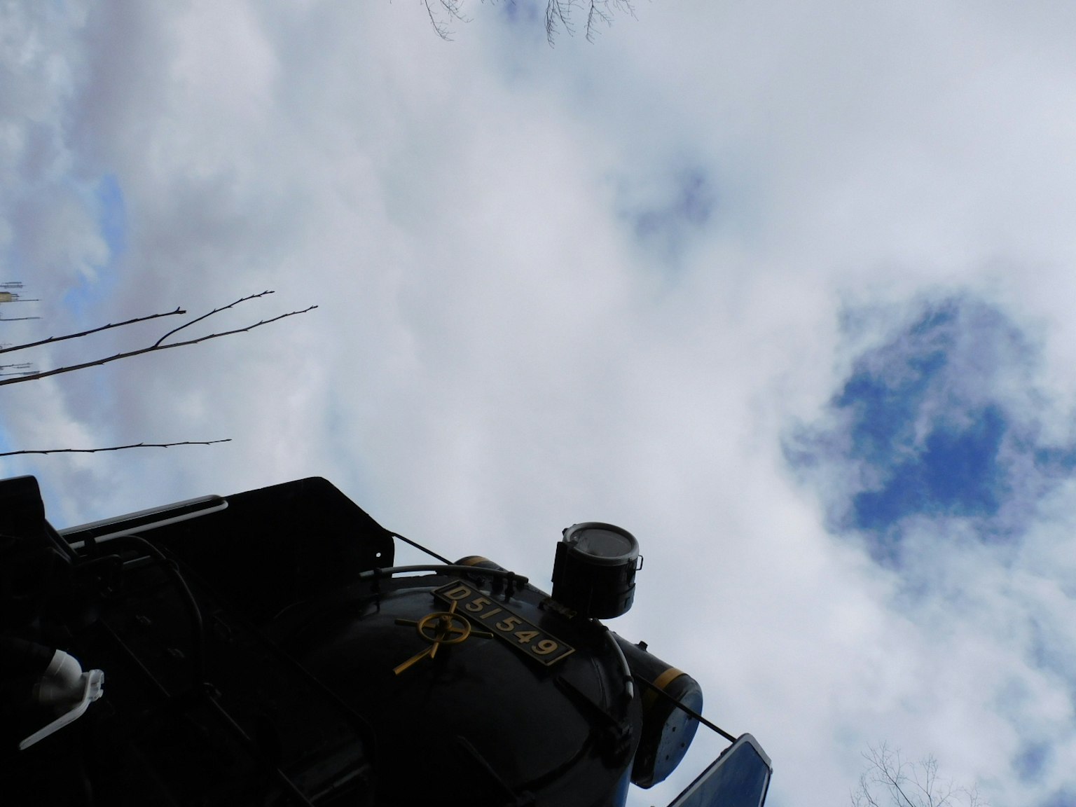 Gambar yang menunjukkan bagian dari mesin dengan latar belakang langit biru dan awan