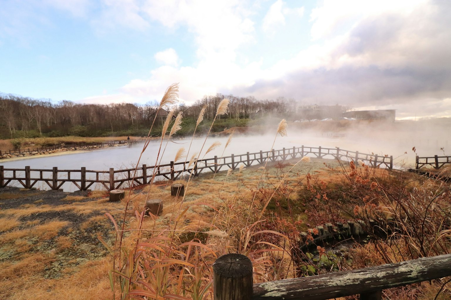 Scenic view of a quiet lake with rising steam from hot springs wooden fence and dry grassland
