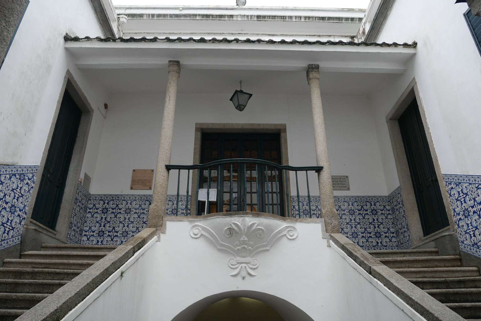 Ingresso principale di un edificio con pareti bianche, scale e balcone