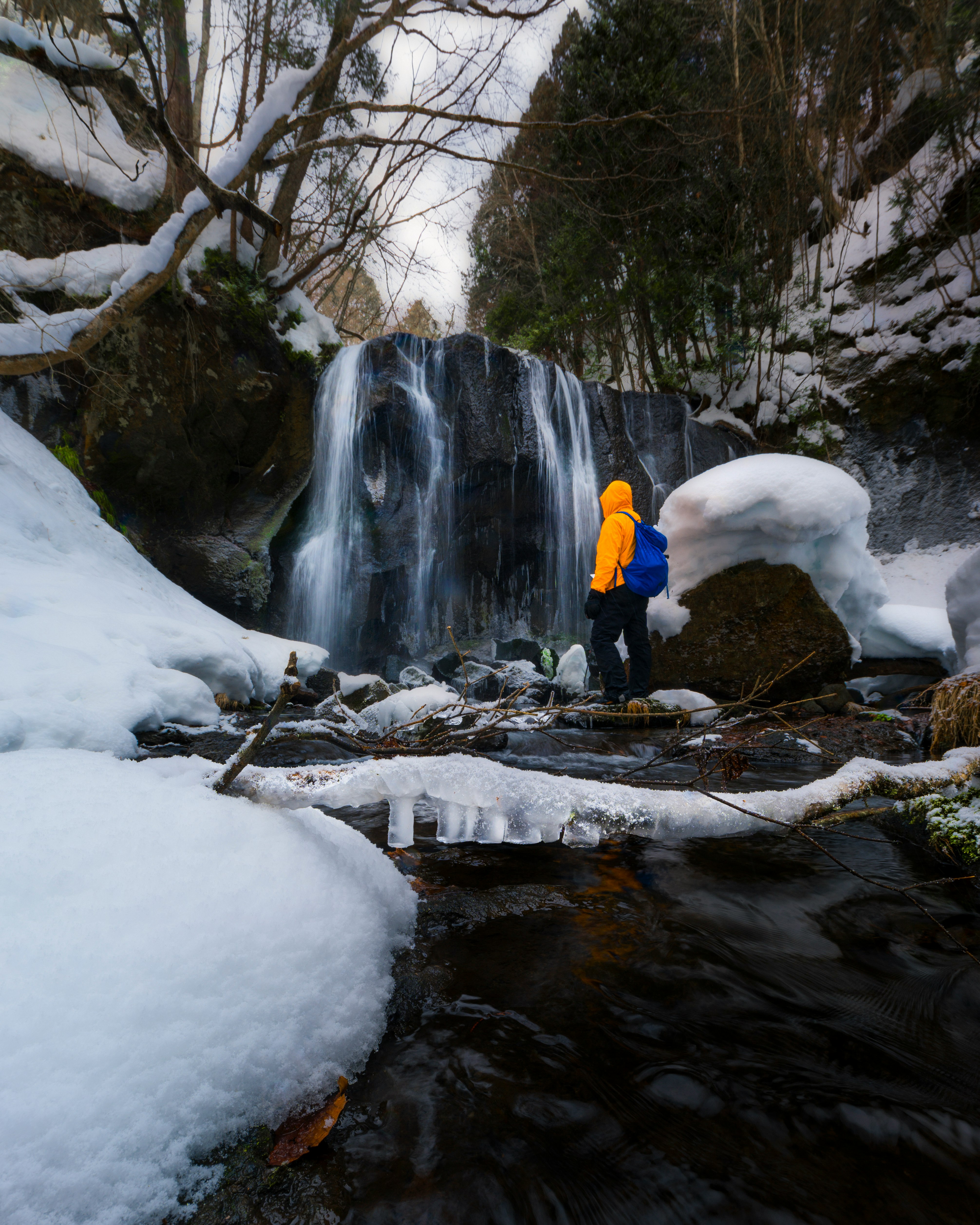 Une personne en tenue d’hiver près d’un ruisseau enneigé et d’une cascade