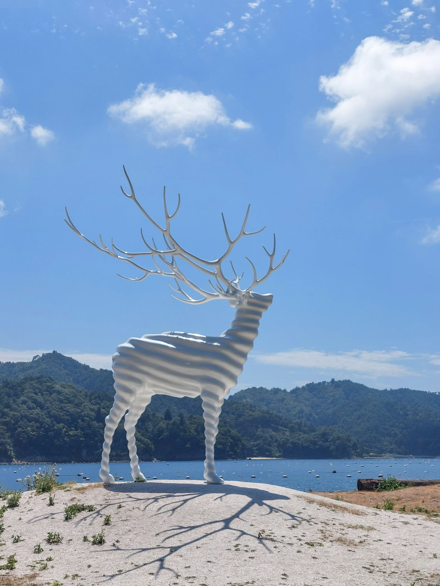 Patung rusa putih berdiri di bawah langit biru dikelilingi oleh pegunungan dan danau