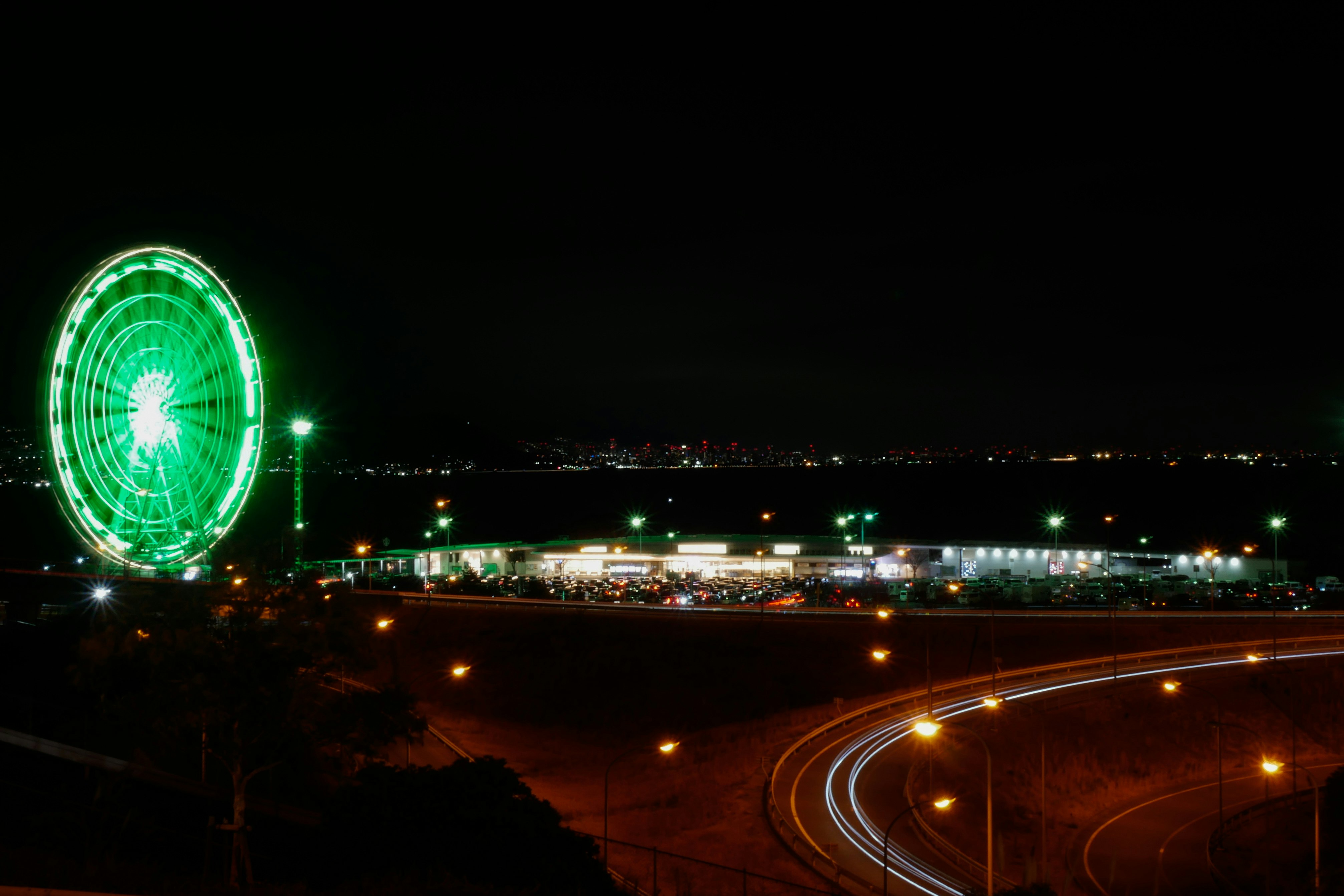 夜の観覧車と湾岸の夜景、車のライトが流れる風景