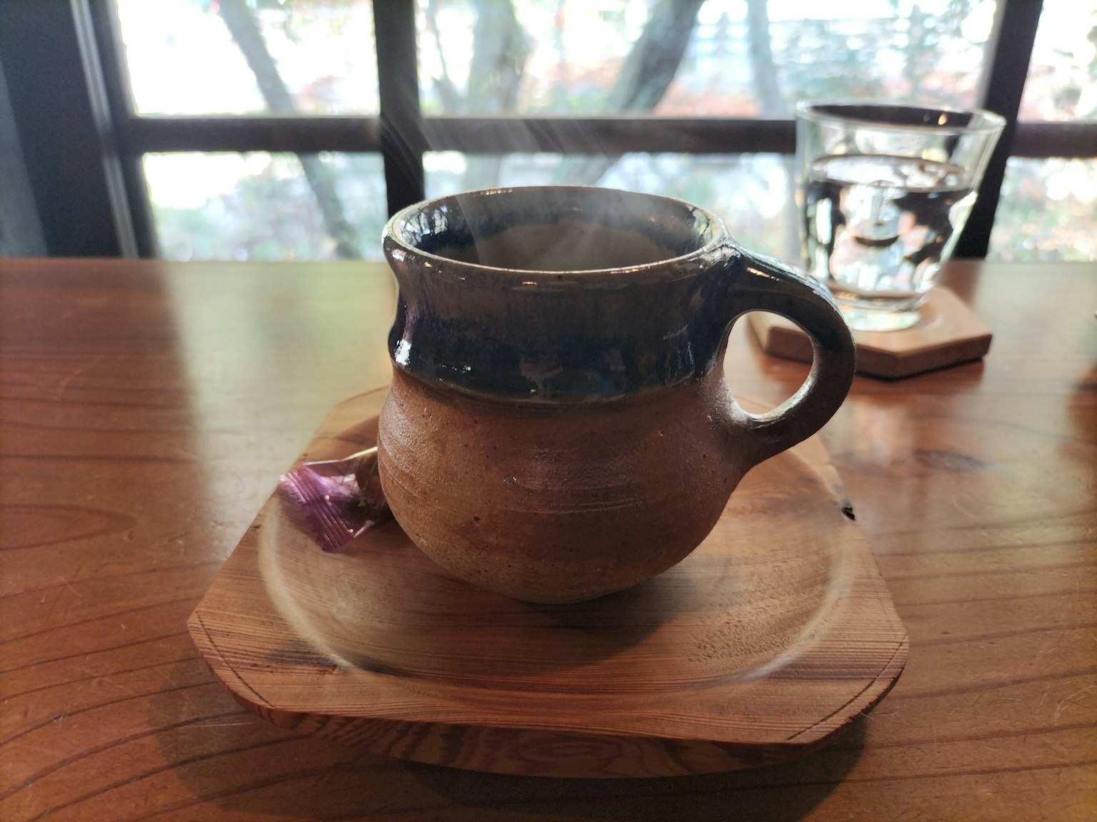 Una taza de cerámica humeante sobre un plato de madera con una flor delicada al lado