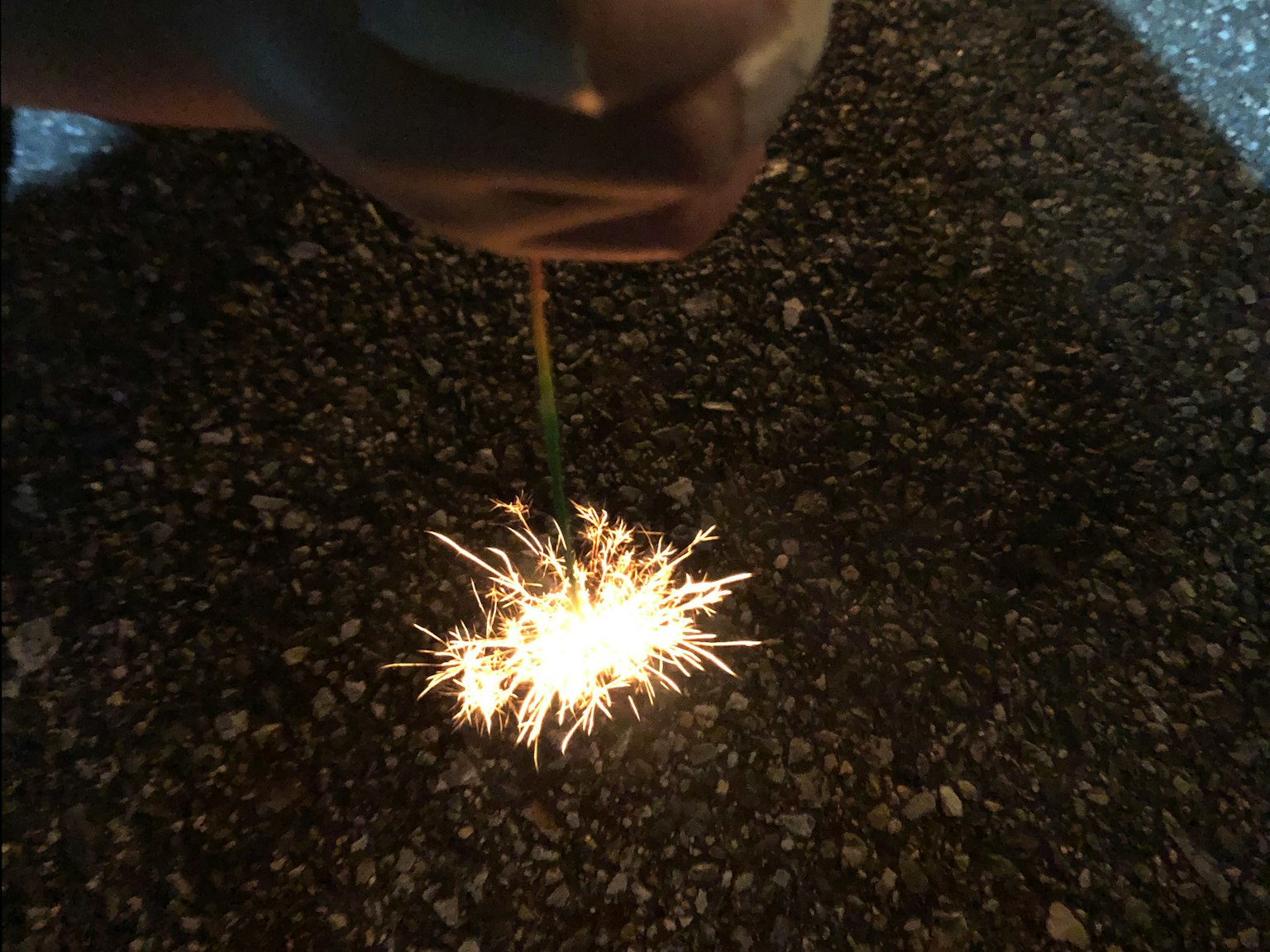A sparkler being held in hand glowing against a dark background