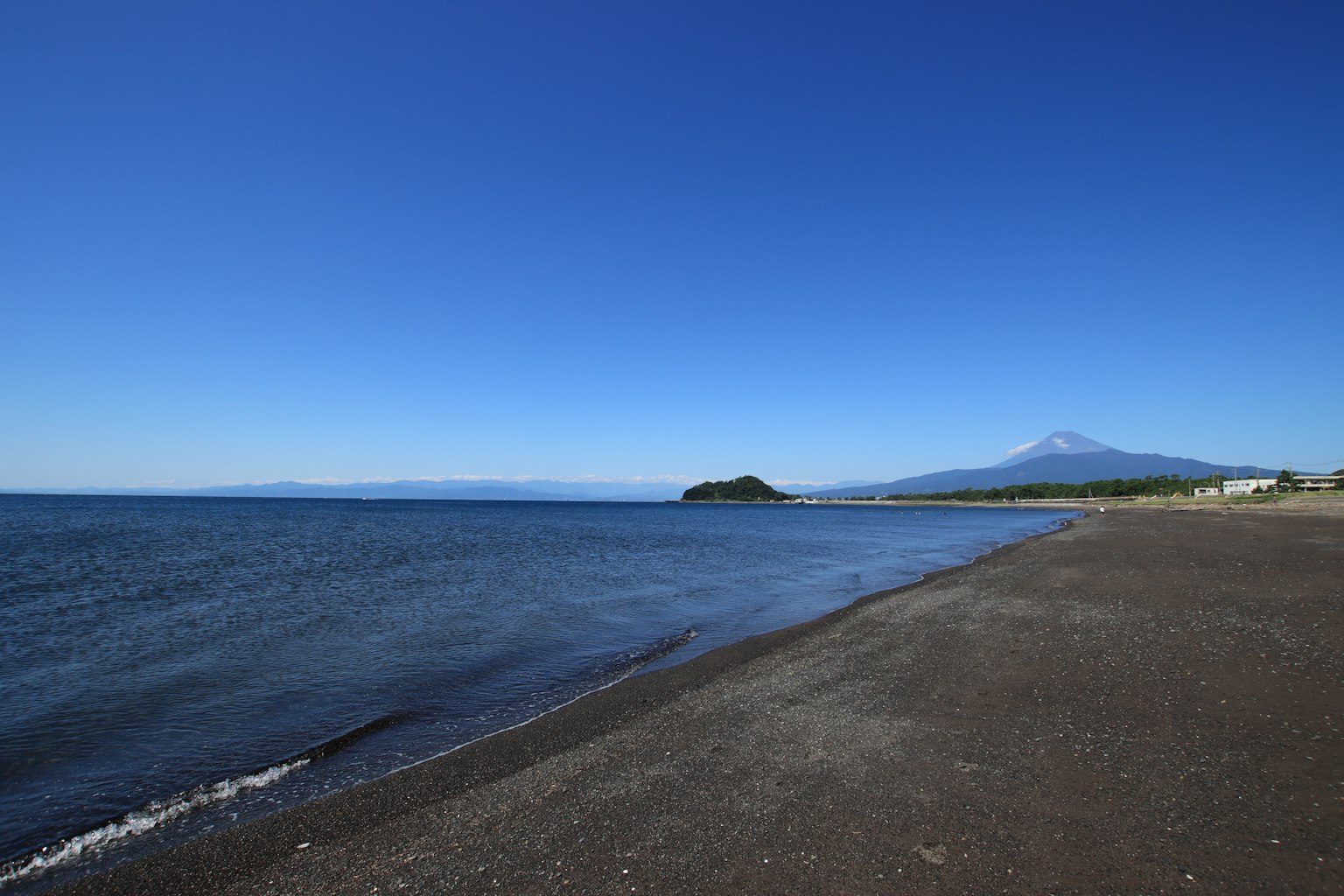 Malersiche Aussicht auf blauen Himmel und Meer schwarzer Sandstrand mit einem Berg in der Ferne