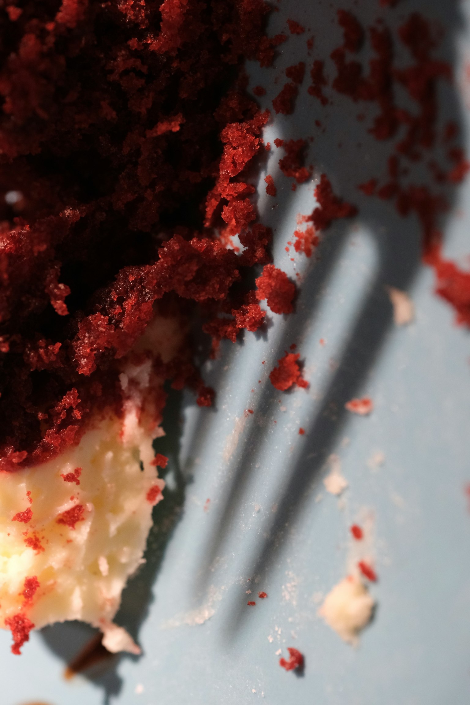 Primer plano de migas de pastel de terciopelo rojo con la sombra de un tenedor en un plato azul