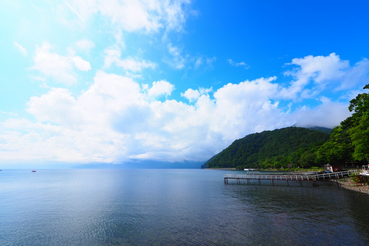 Ruhiger See mit blauem Himmel und weißen Wolken grüne Hügel im Hintergrund