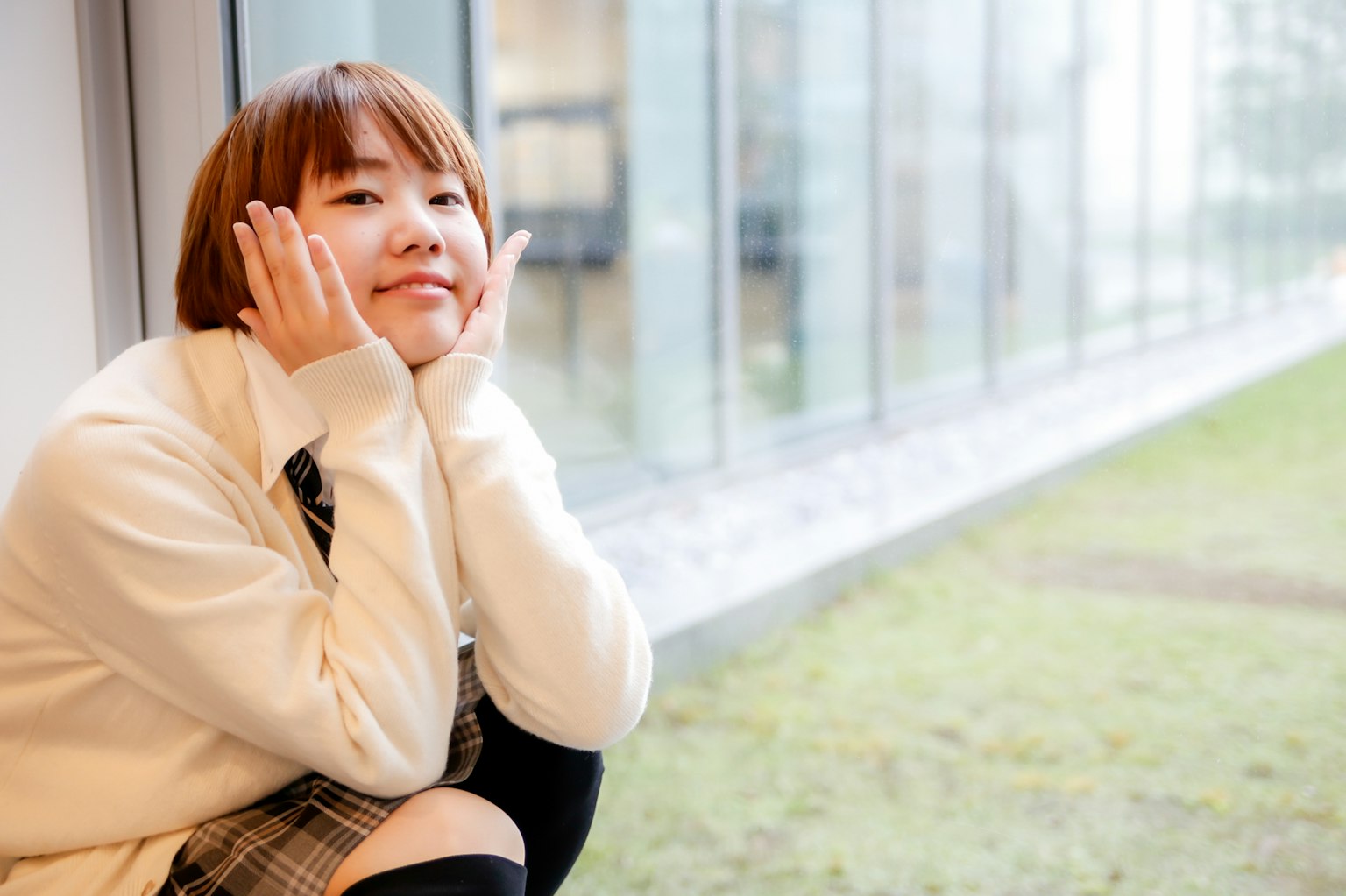 Ritratto di una giovane donna seduta vicino alla finestra con un sorriso Indossa un maglione bianco in un ambiente luminoso con luce naturale