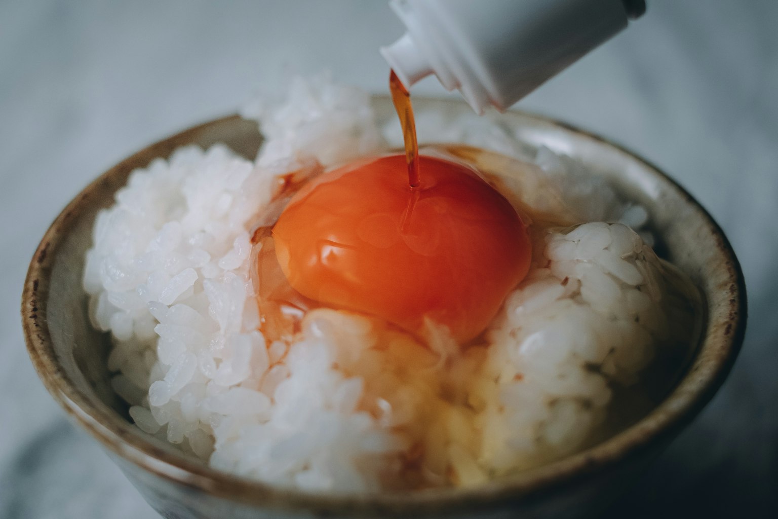 Un tazón de arroz cubierto con una yema de huevo cruda rociada con salsa de soja