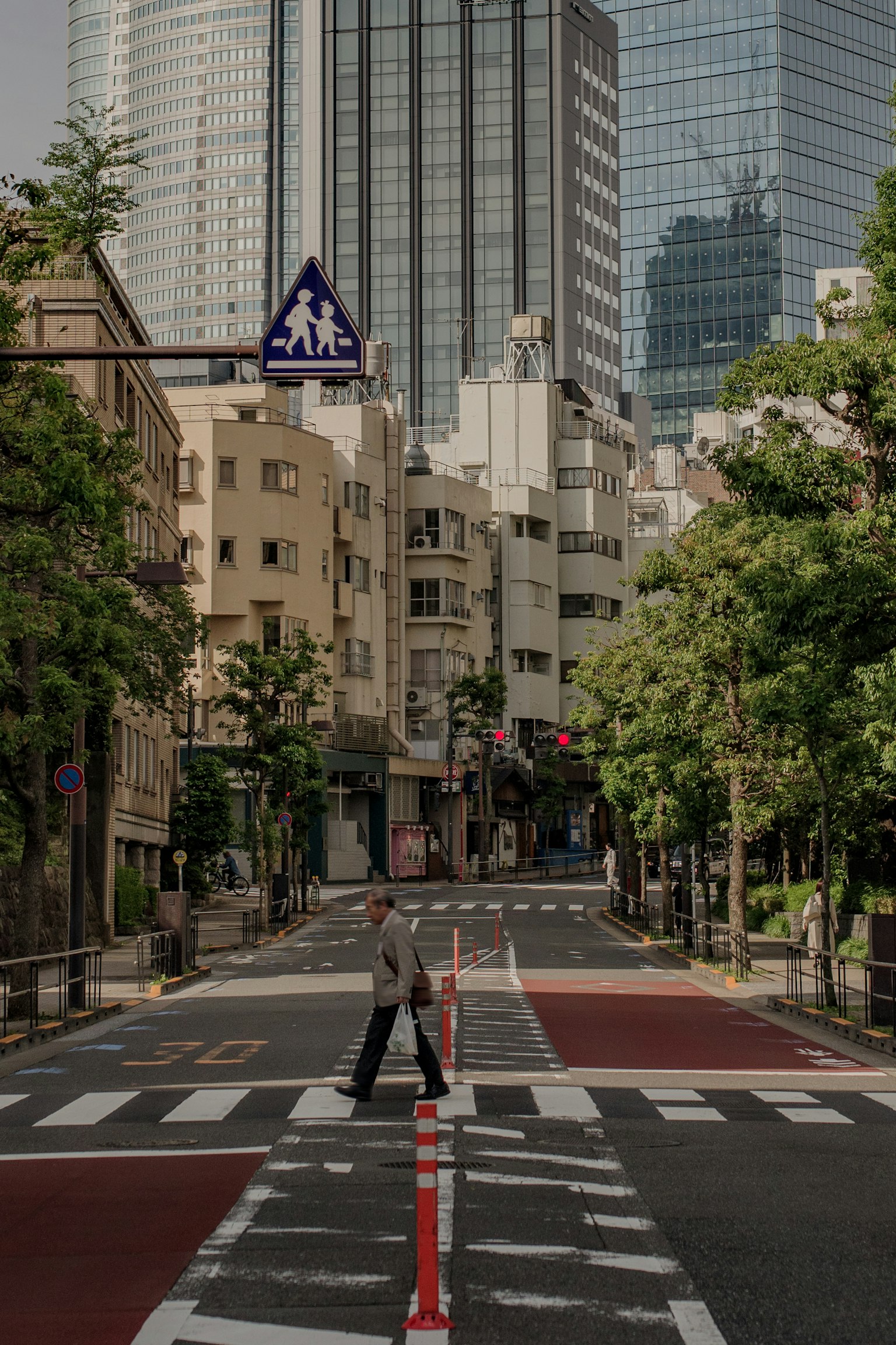 城市景觀中有人過馬路，背景是高樓和綠色街樹
