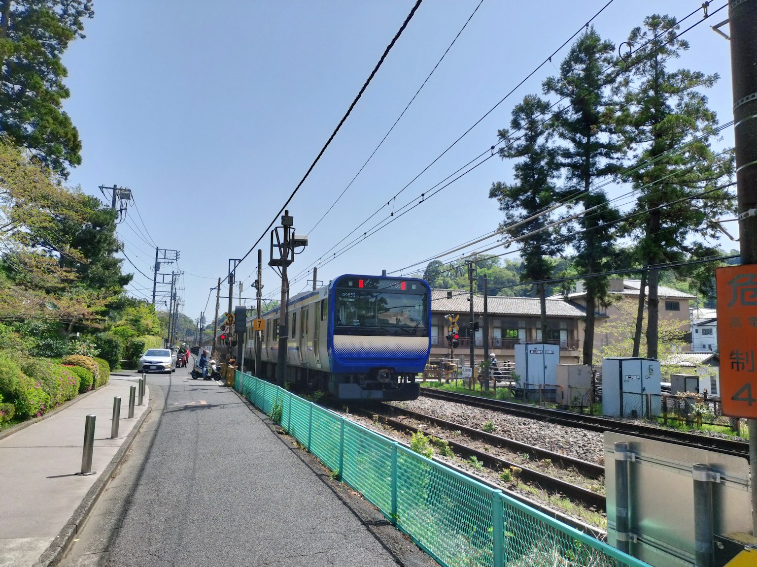 Blue train passing by along the tracks with green trees and blue sky