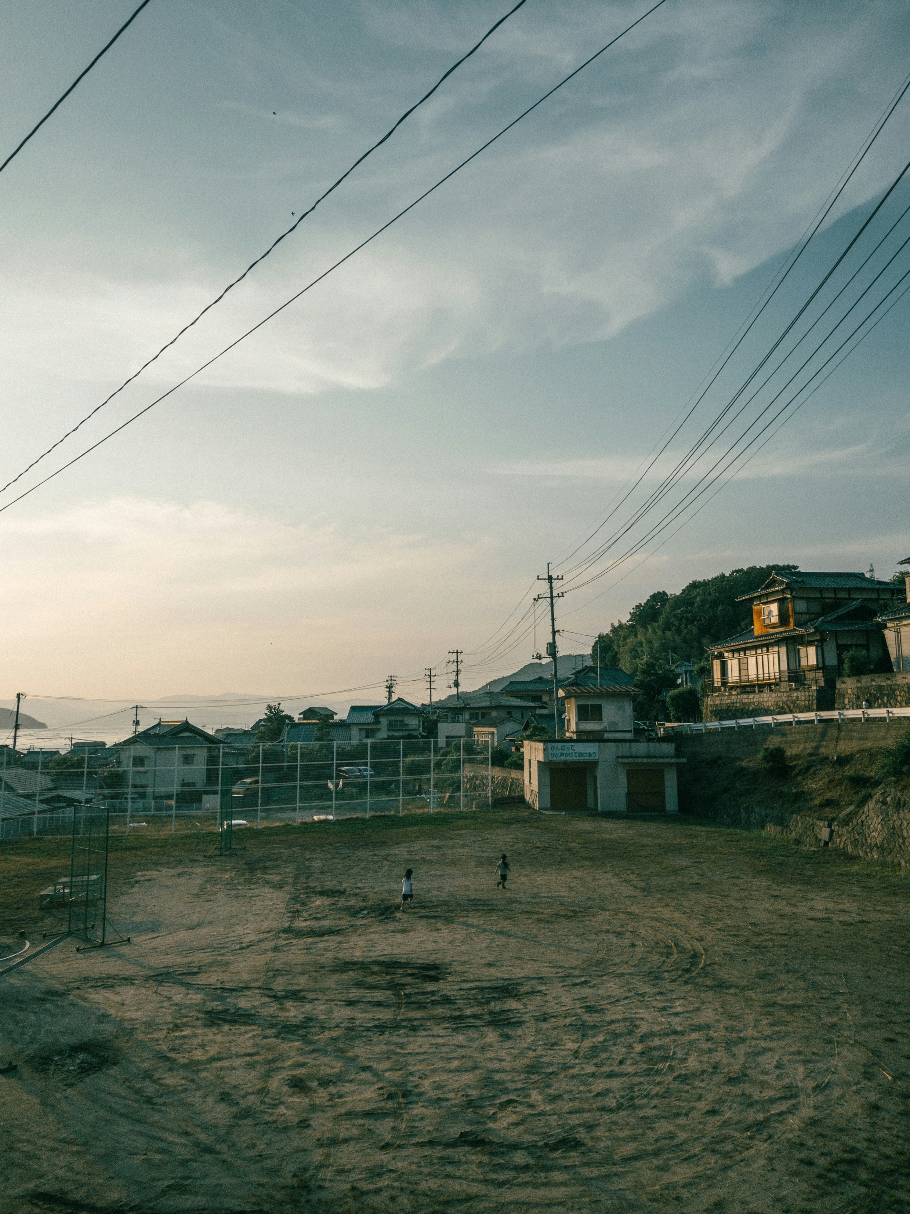 郊外の草地とフェンス、夕暮れの空に電線が伸びる風景