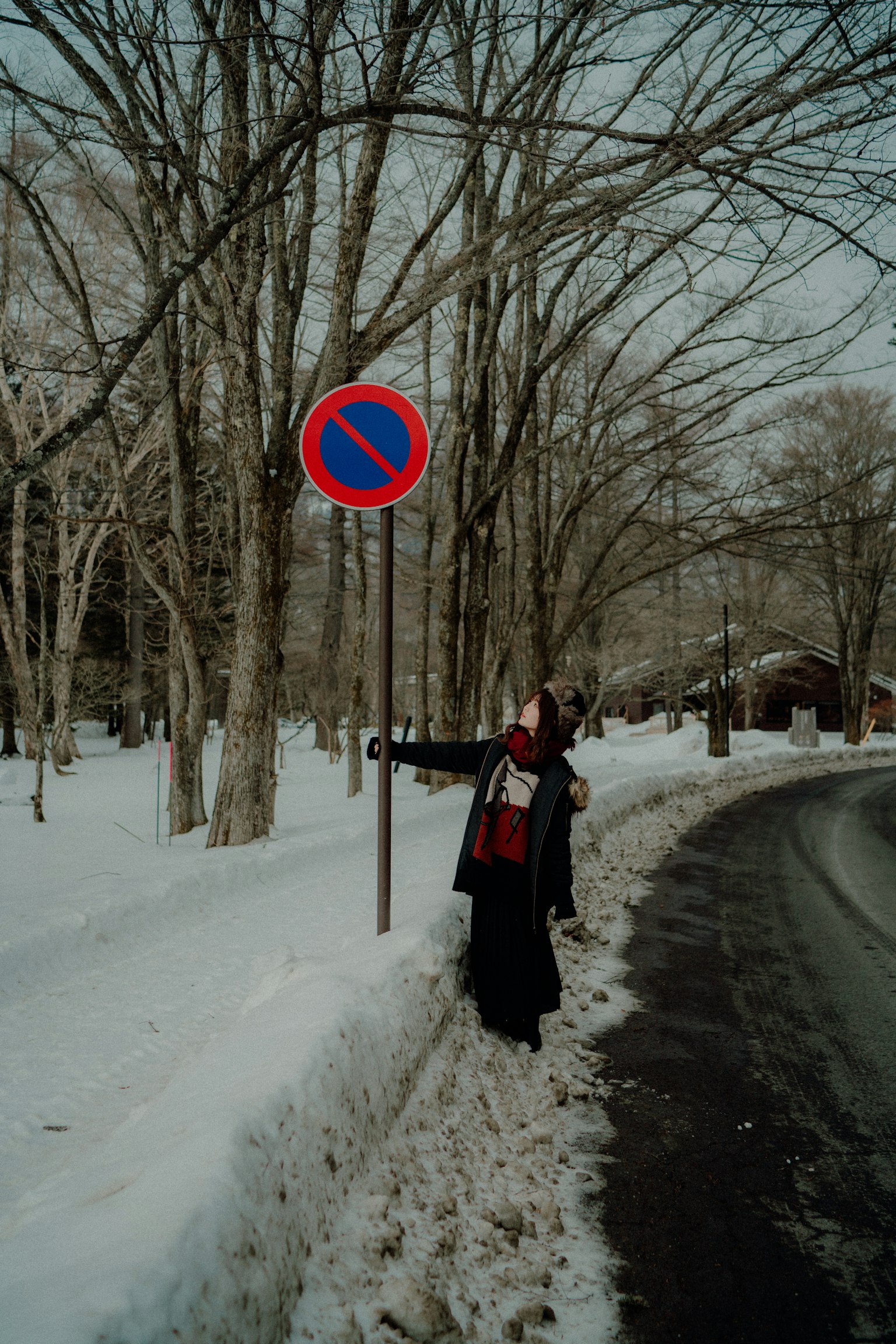 一个人站在被雪覆盖的道路旁边，旁边有一个禁止停车的标志