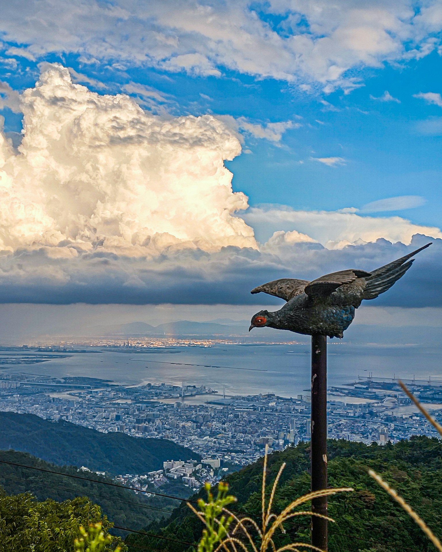 Paysage montagneux avec une sculpture d'oiseau s'envolant contre un ciel bleu et des nuages