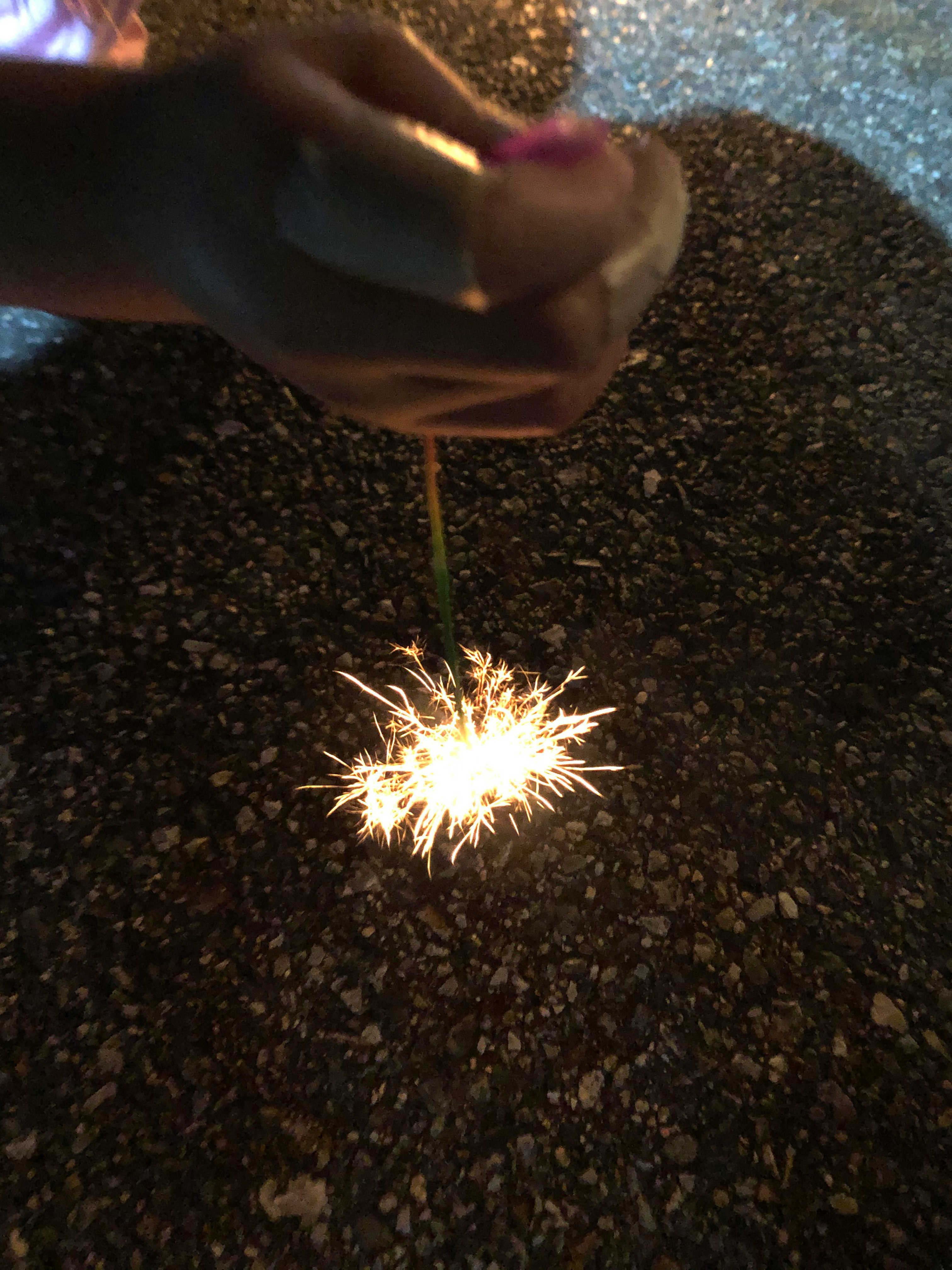 mano che tiene uno sparklers che sprigiona scintille su una strada notturna