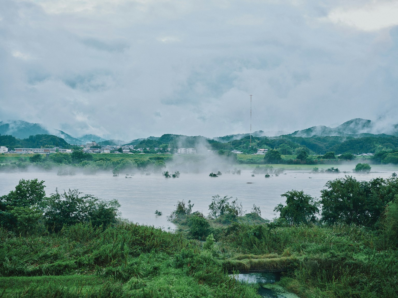 Misty river landscape with lush greenery and distant hills