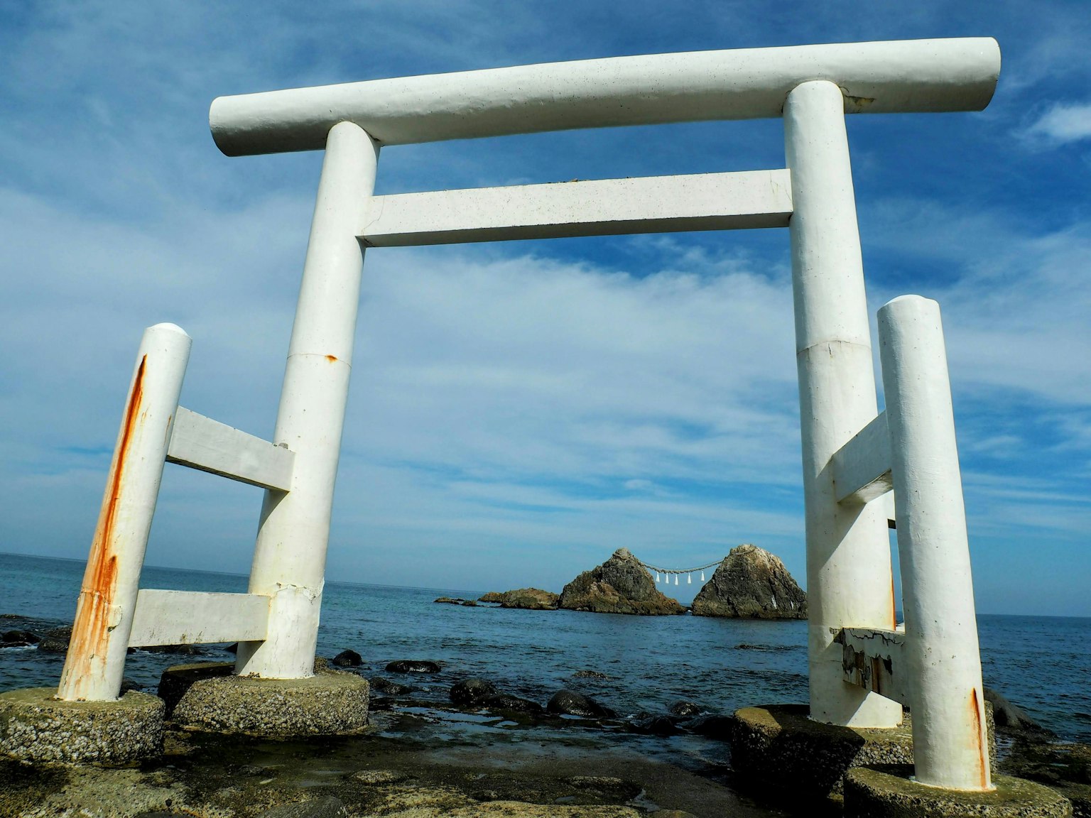 Gerbang torii putih dengan pulau berbatu dan langit biru