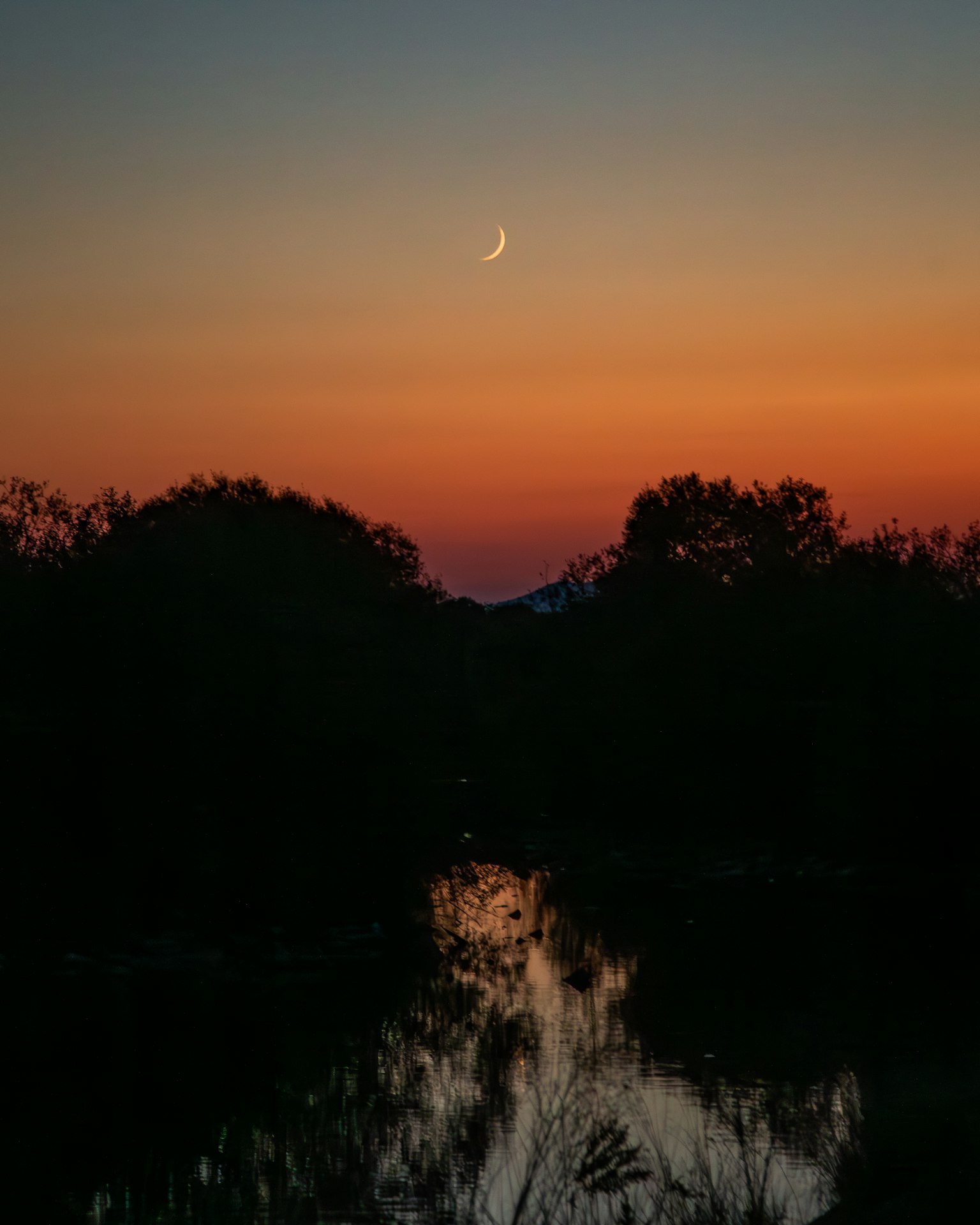 Une lune croissante dans le crépuscule au-dessus d'un lac paisible