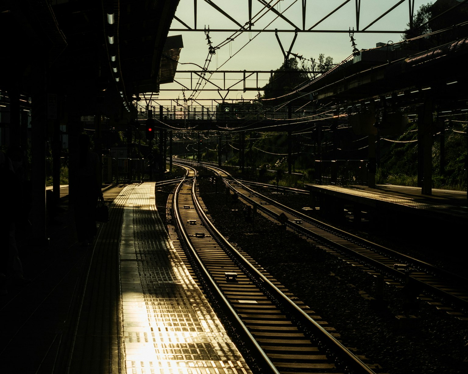 Silhouette of tracks and overhead wires viewed from a train station platform
