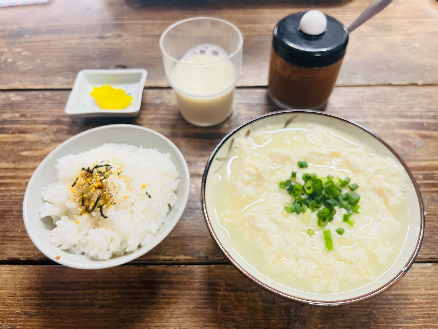 一碗溫暖的湯，上面撒有青蔥，旁邊有一碗米飯，放在木桌上